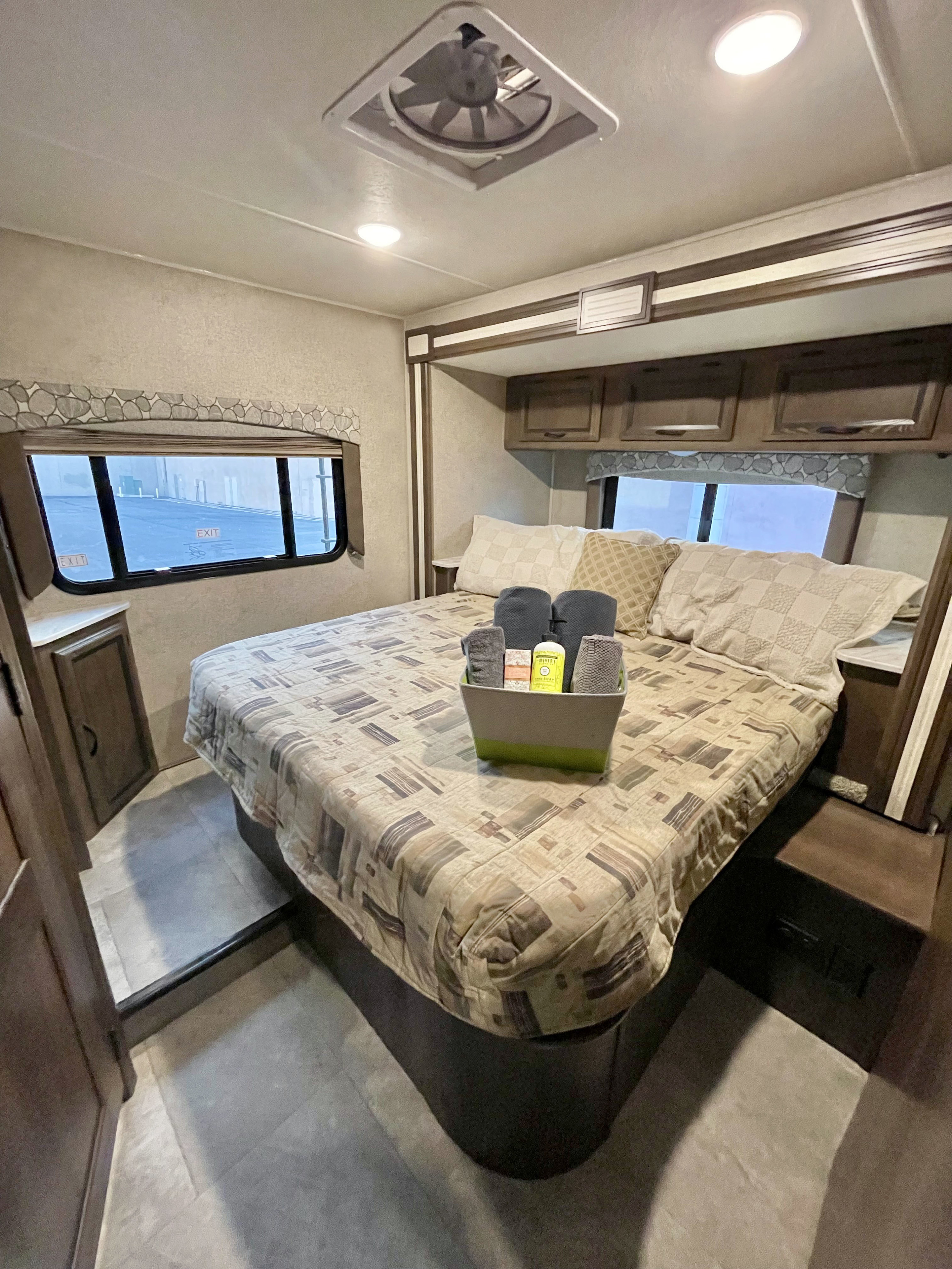 Cozy RV rental bedroom with patterned bedding, overhead cabinets, window view, and toiletries basket on the bed.. Forest River Coachmen Freelander 2019