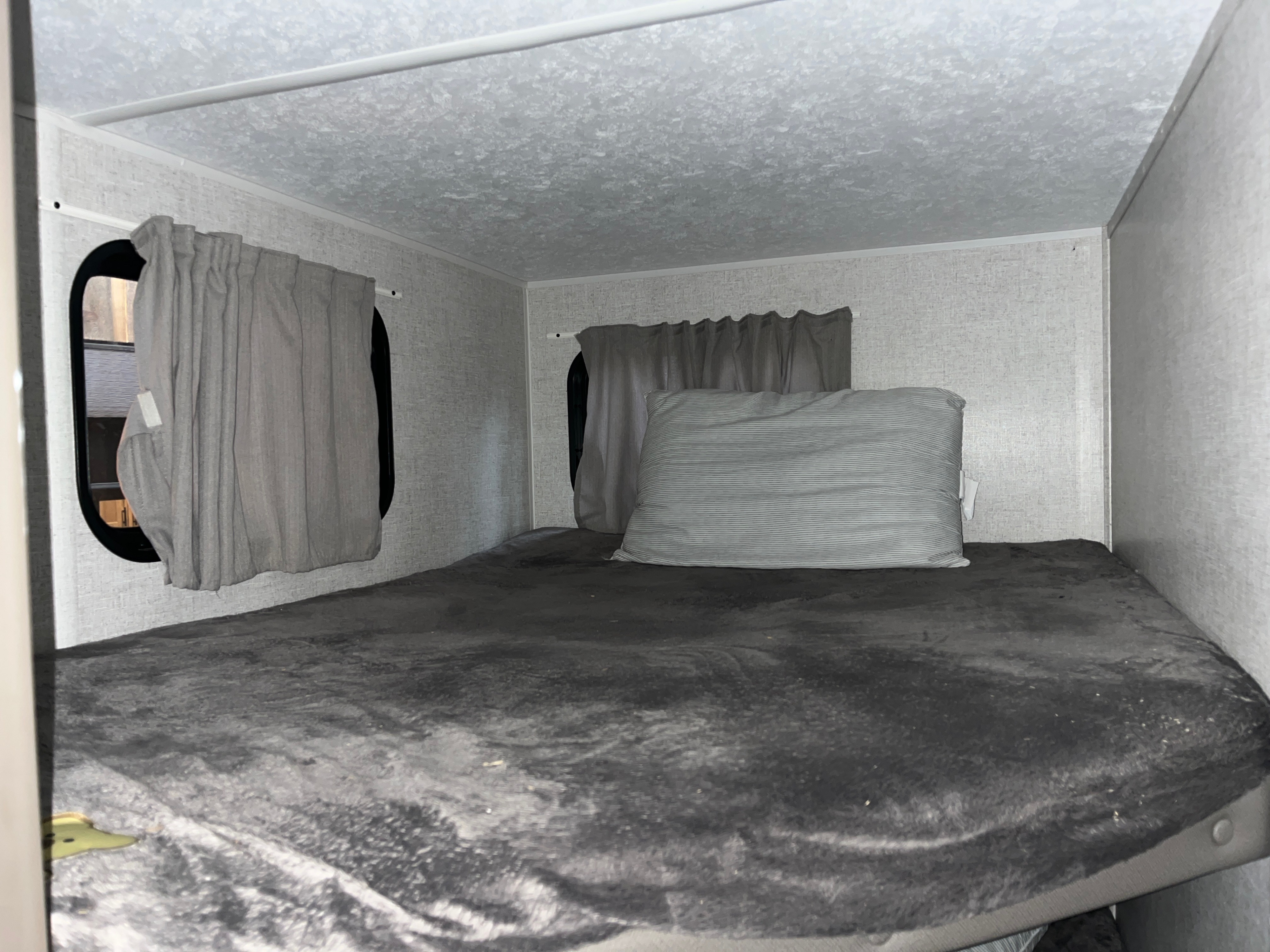 RV rental bunk bed: a cozy sleeping space with dark blanket, striped pillow, and window curtains.. Forest River EvoFS 2021