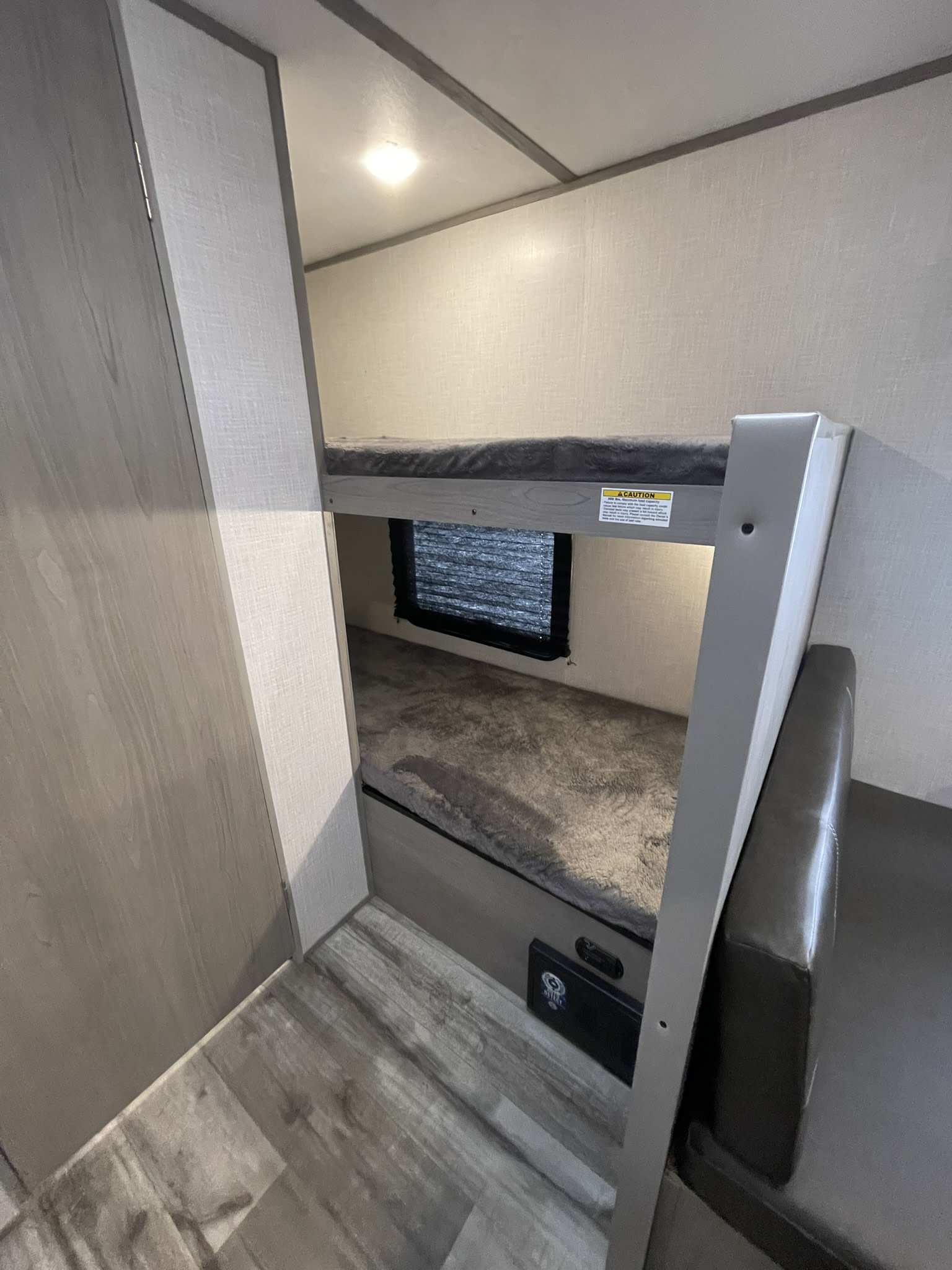 Cozy RV rental interior with dual bunk beds, a small window, ceiling light, and brown leather seating.. Dutchmen Coleman Lantern 2022