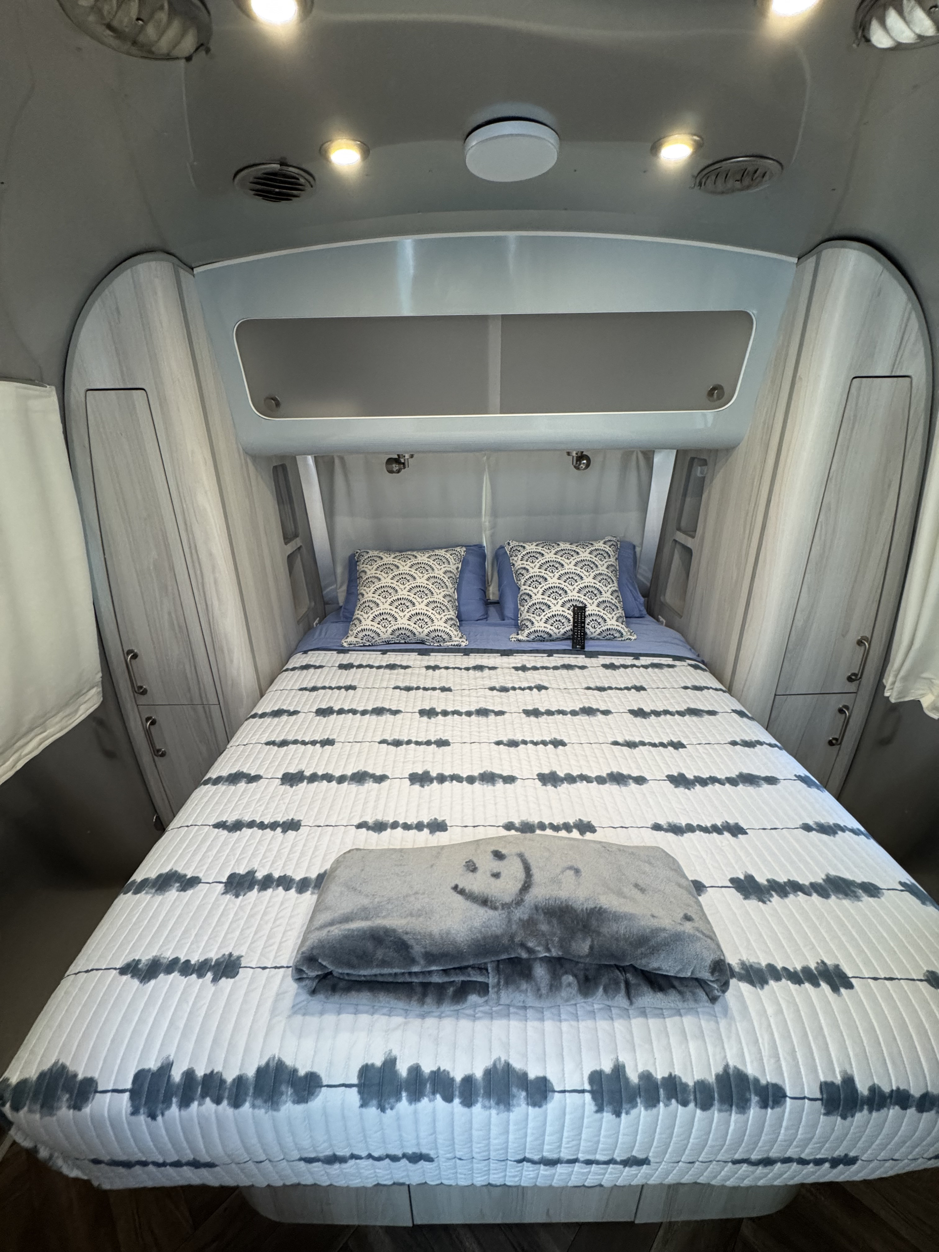 Inside a comfortable RV rental: compact bedroom with patterned bedding, built-in storage, and overhead lighting.. Airstream International 2022