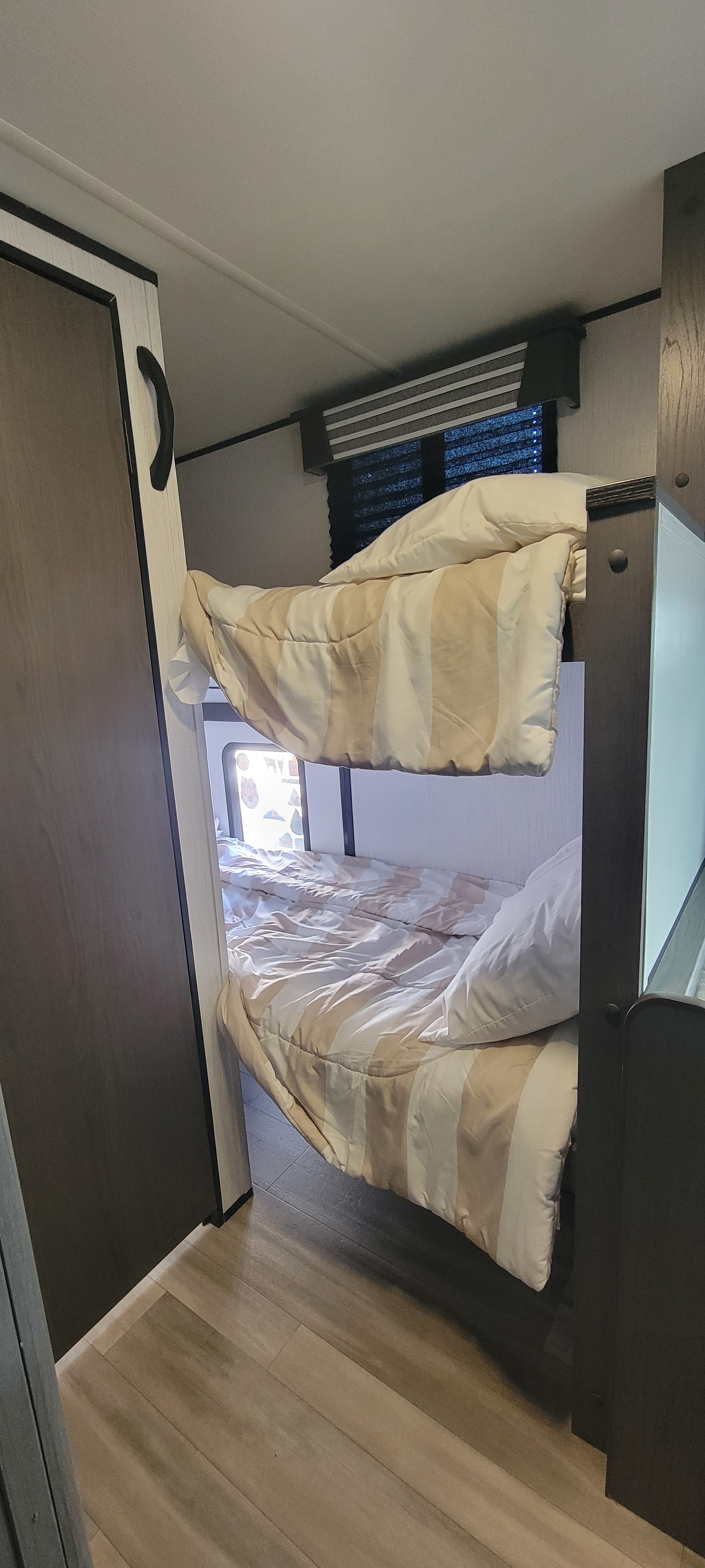 Inside a clean RV rental: two compact bunk beds with striped bedding and pillows, next to a window with blinds.. Heartland RVs Mallard Pathfinder 2022