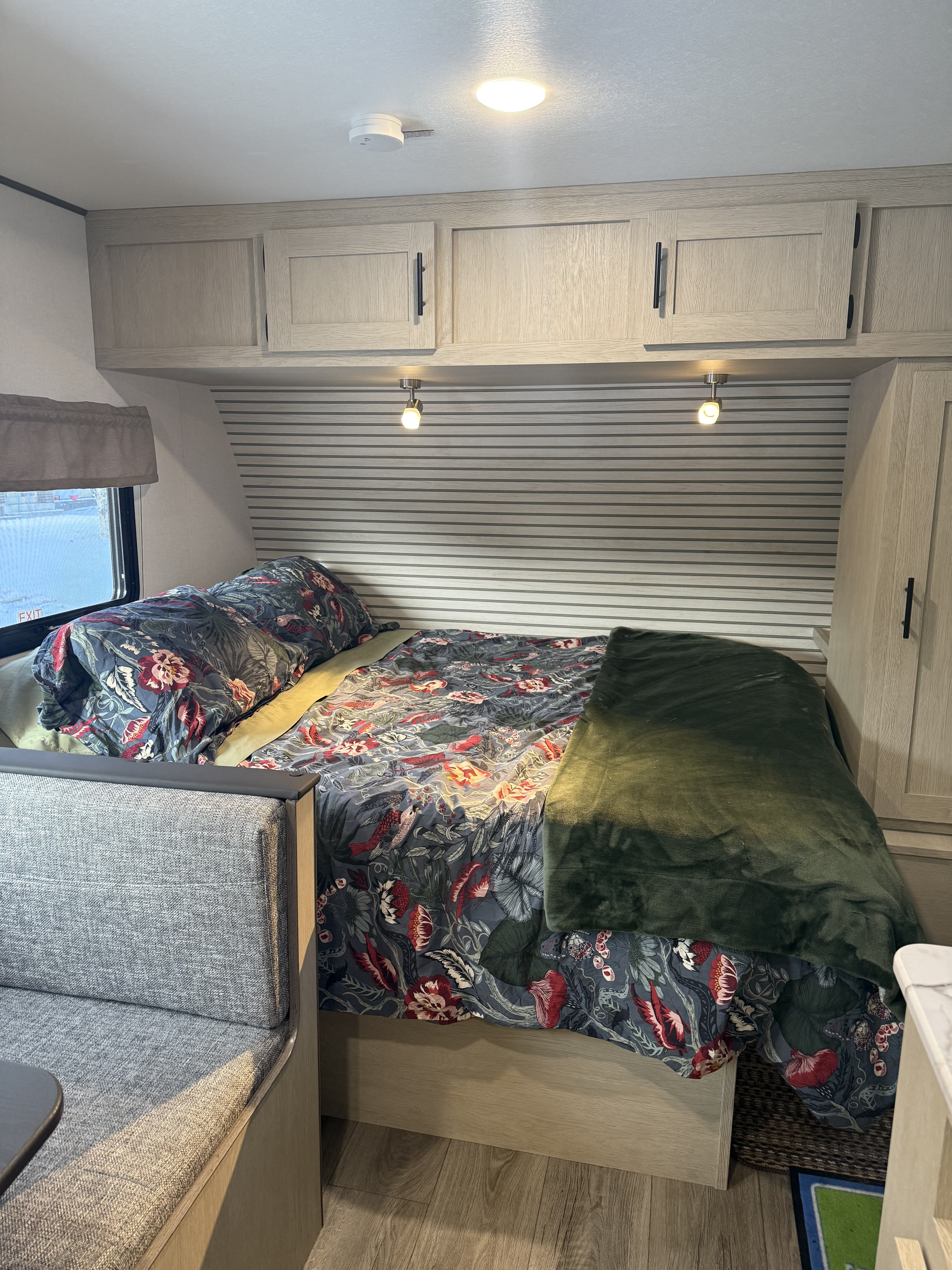 Cozy RV rental interior featuring a floral bed, gray dinette, and overhead cabinets for a comfortable stay.. Coachmen Shasta compact 18 bunk house 2025