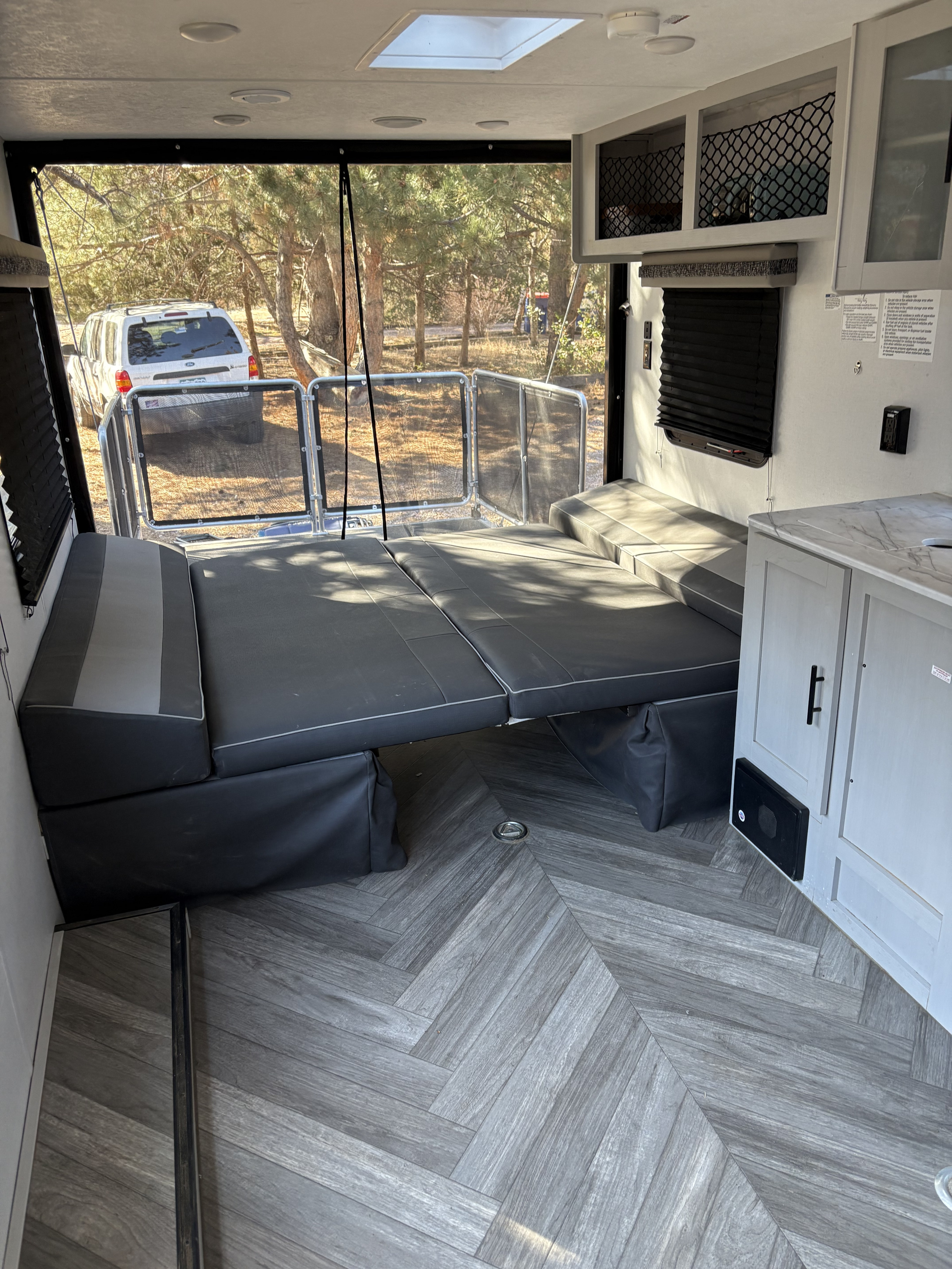 Spacious RV rental interior featuring a large convertible bed, modern herringbone flooring, and a screened back opening.. Forest River Fxs Wildwood 2021