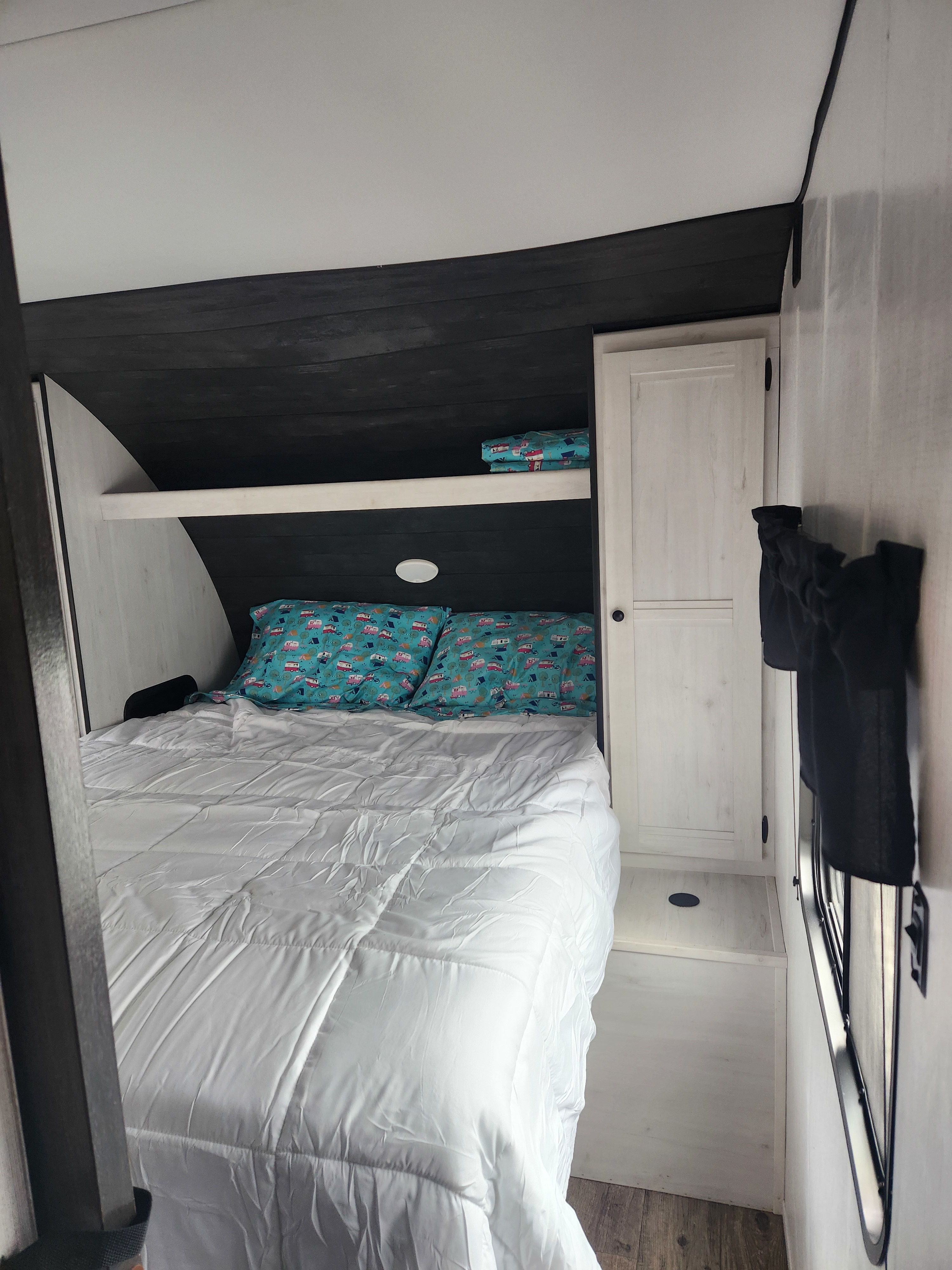 Compact RV rental bedroom with a white bed, unique camper-print pillows, and built-in storage.. Heartland RVs Trail Runner 2022