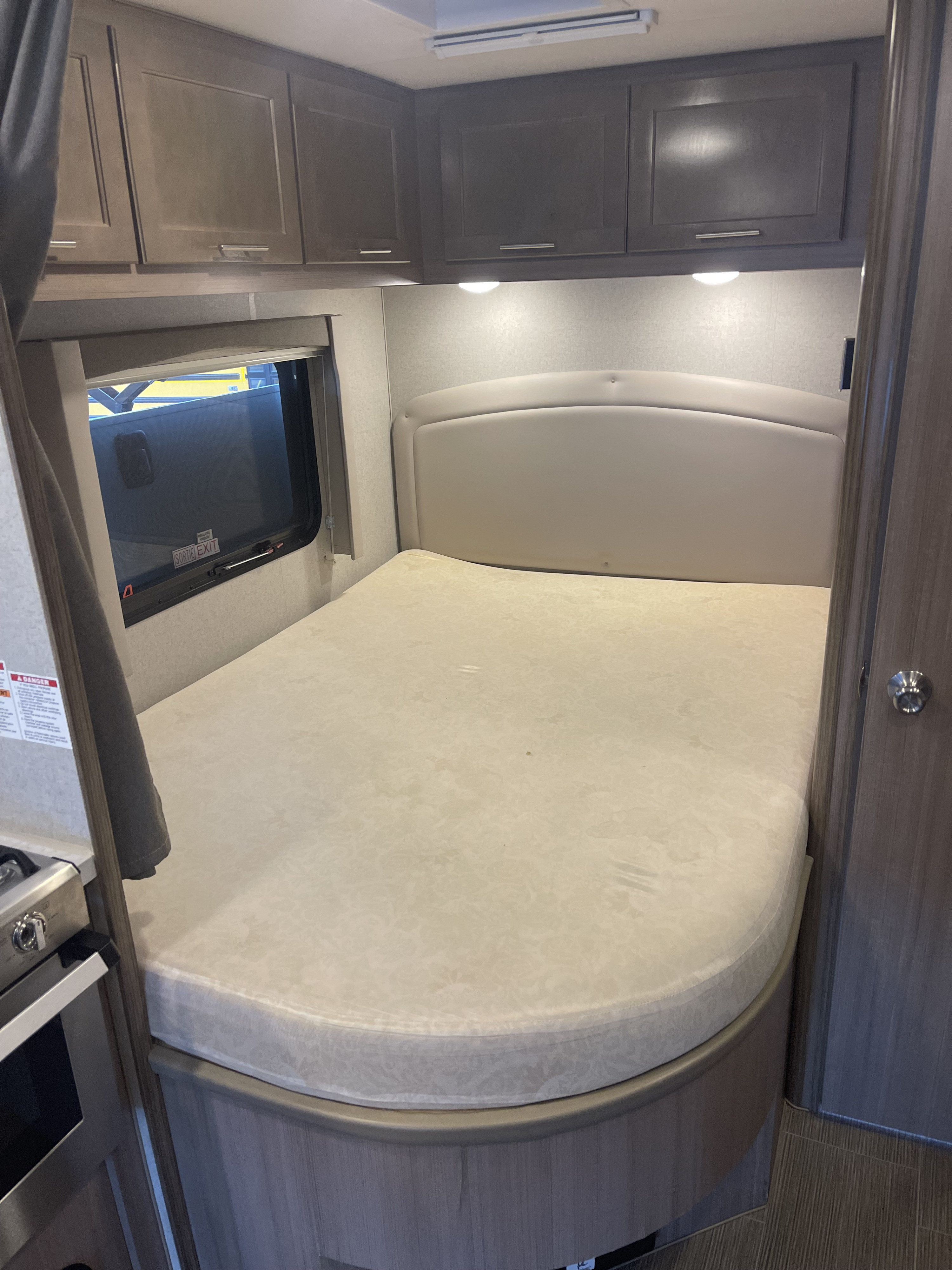 Inside an rv rental, featuring a cozy bedroom with a comfortable rounded bed, overhead cabinets, and a window with an emergency exit.. Adventurer 24DS 2021
