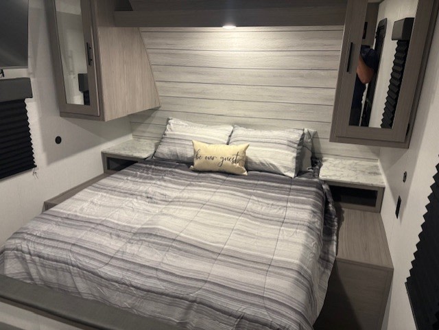 Comfortable RV rental bedroom with striped bedding, 'be our guest' pillow, storage, and nightstands.. Coleman Lantern 2024