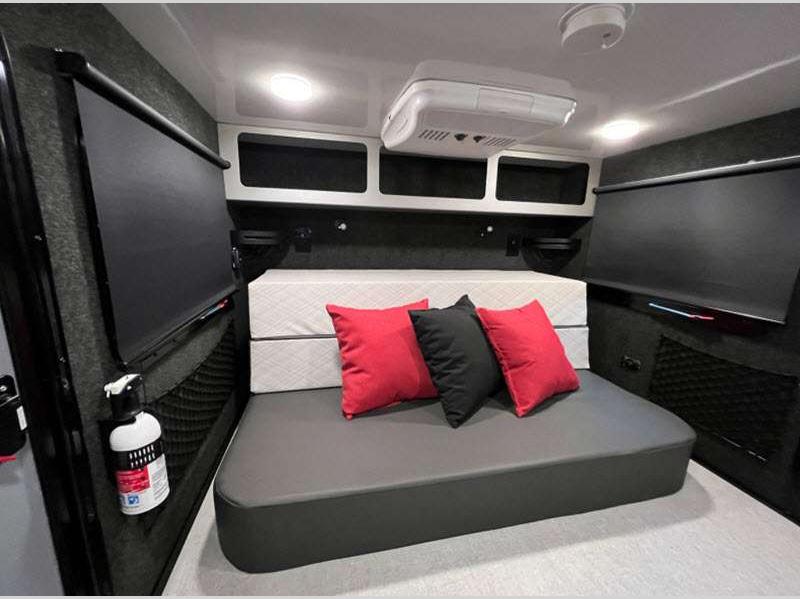 Cozy RV rental interior featuring a bed/sofa with pillows, overhead storage, and an AC unit for comfortable travel.. Encore RV ROG 2022