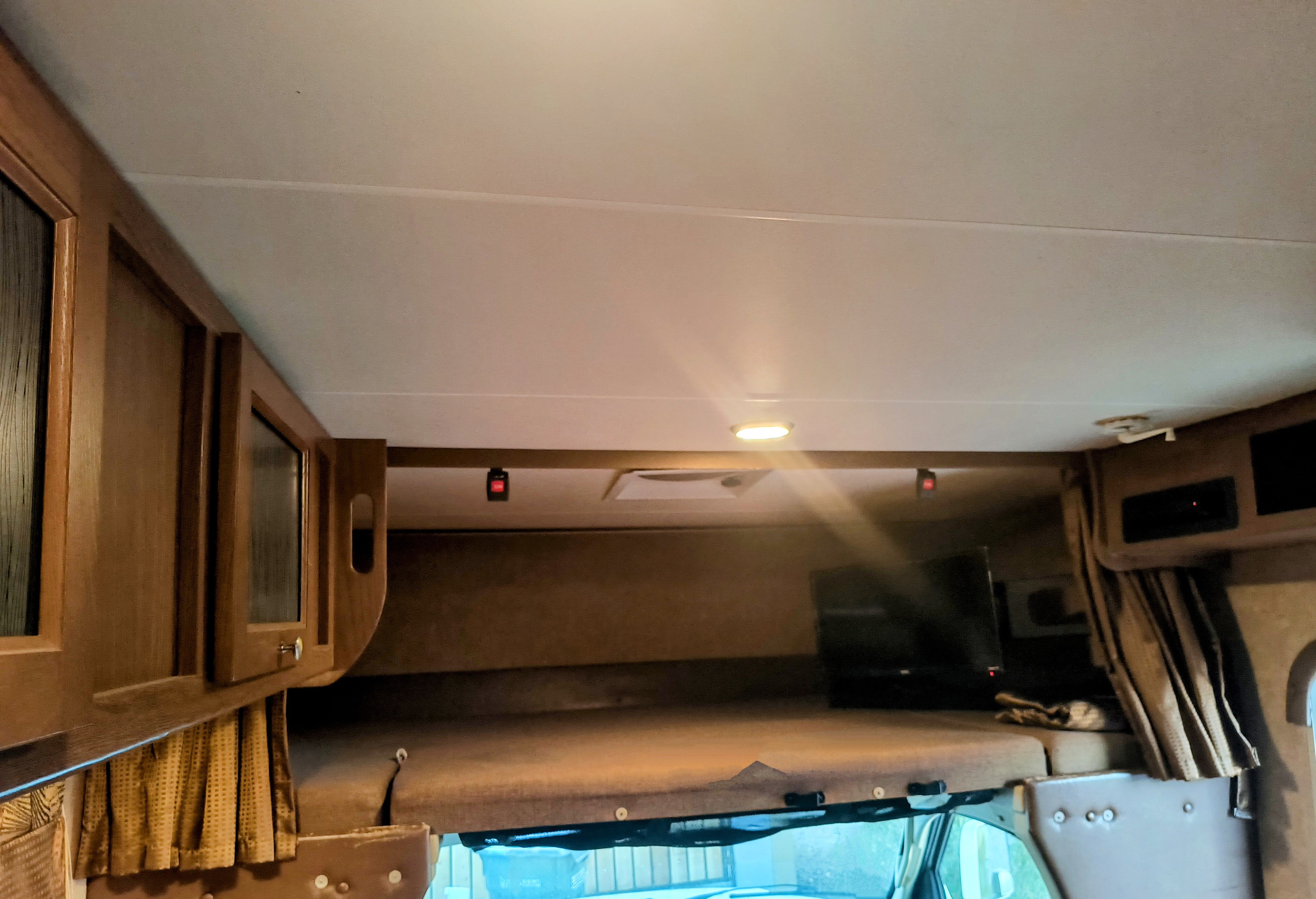 Interior view of an RV rental showing the overhead bunk bed, wooden cabinets, ceiling light, and a mounted TV.. Coachmen Leprechaun 2015