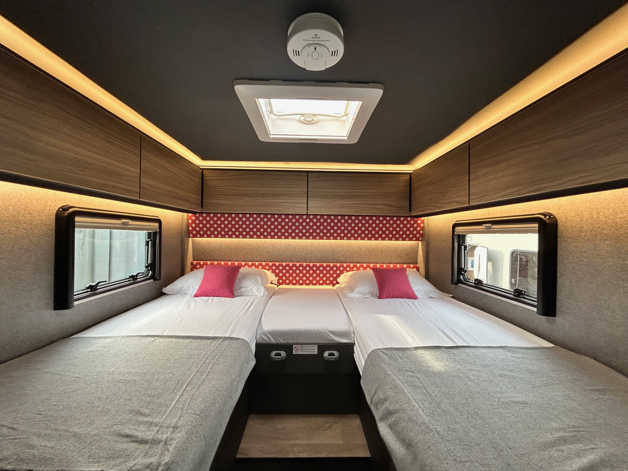 Cozy RV rental bedroom with three beds, windows, overhead storage, ambient lighting, and a skylight.. GlamperRV DBL 2026