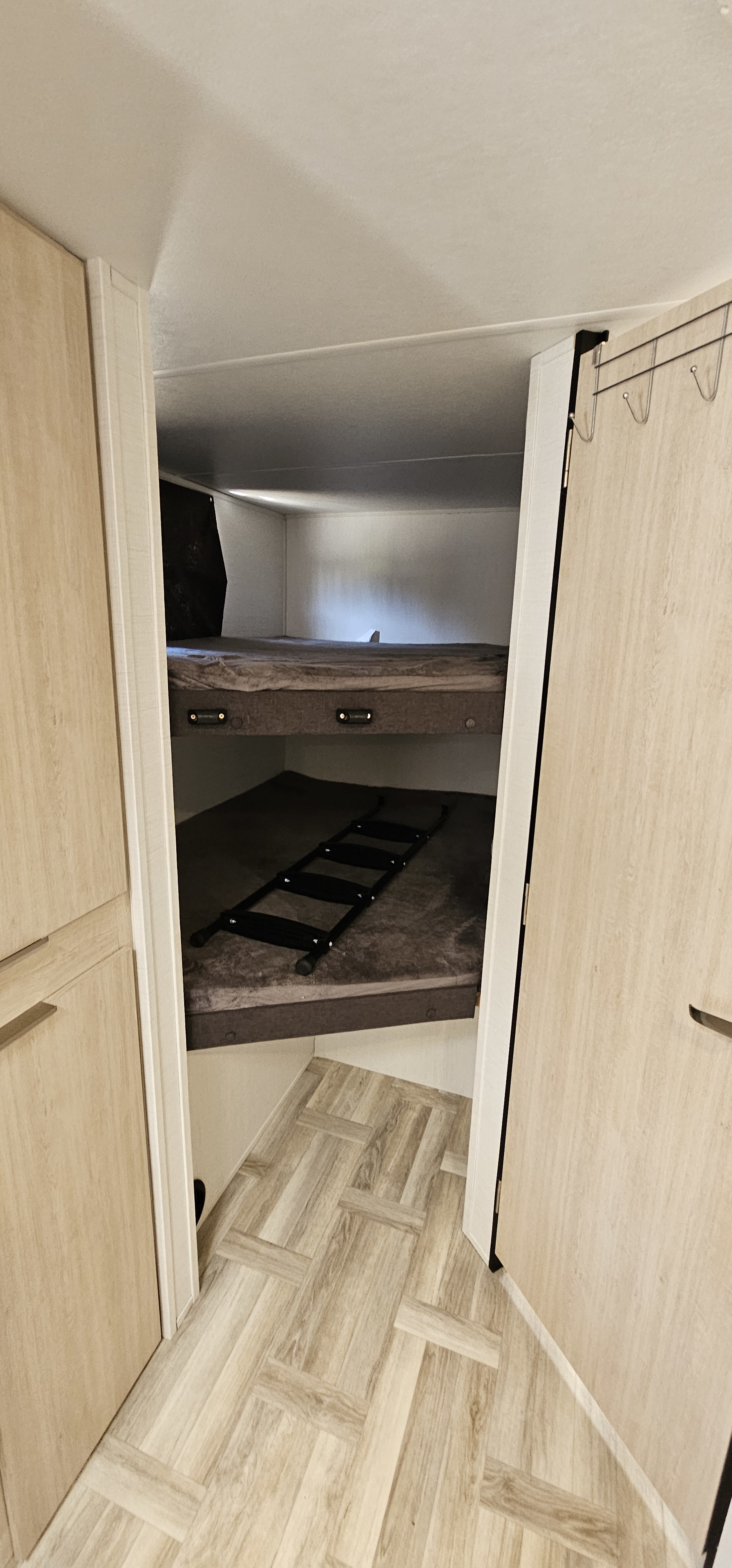 Cozy bunk beds with a ladder in an RV rental. Features light wood cabinetry and herringbone flooring inside.. Prime Time Tracer 2024