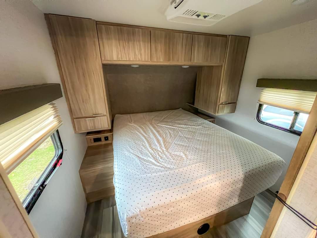 RV rental interior showing a cozy bedroom with a white polka-dot bed, light wood cabinets, and windows with blinds.. Winnebago Minnie Winnie 2021