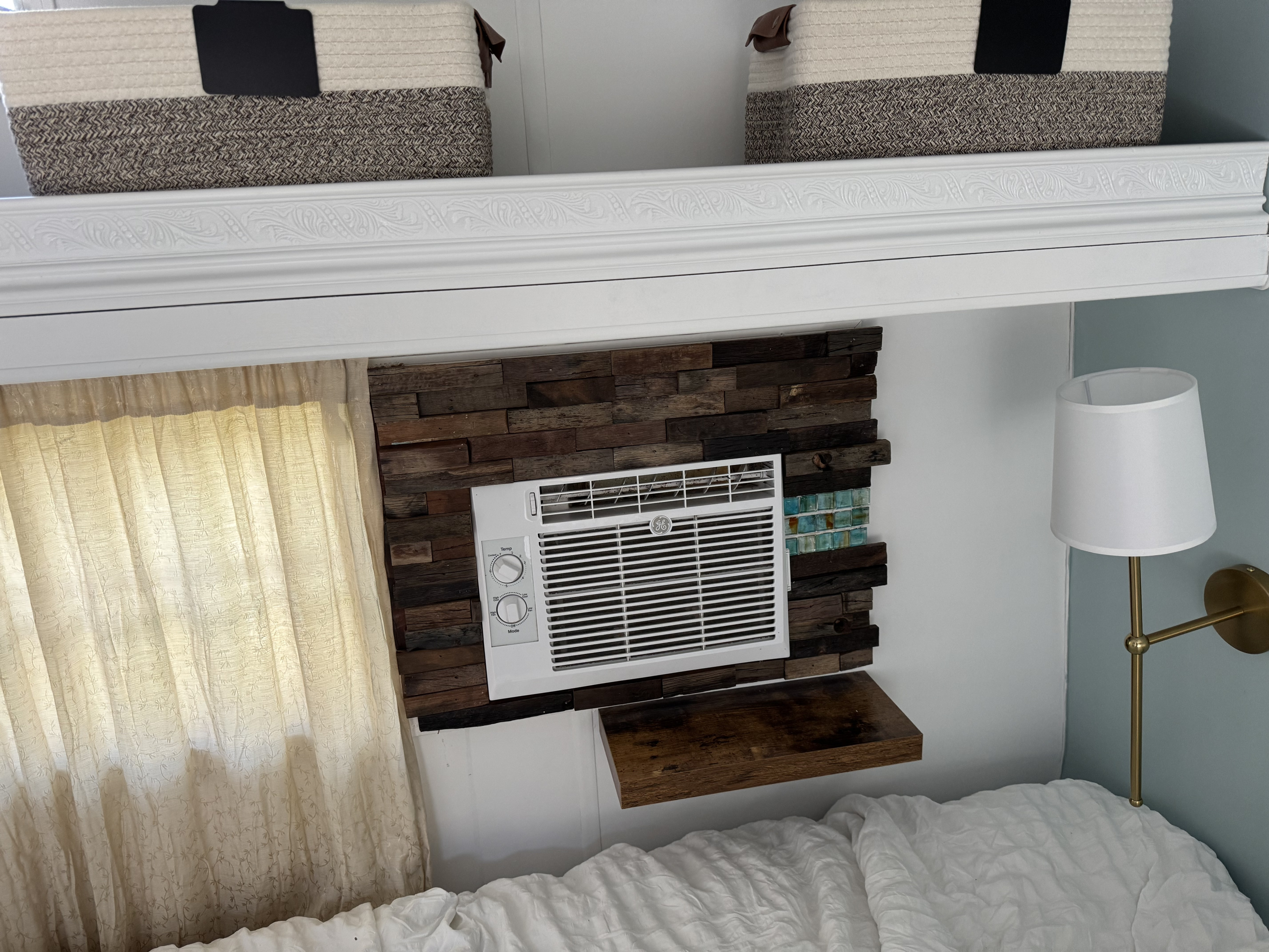Compact RV rental bedroom with a GE AC unit, unique wood accent wall, shelf, woven storage, and comfy bed.. Fleetwood Wilderness Yukon 1987