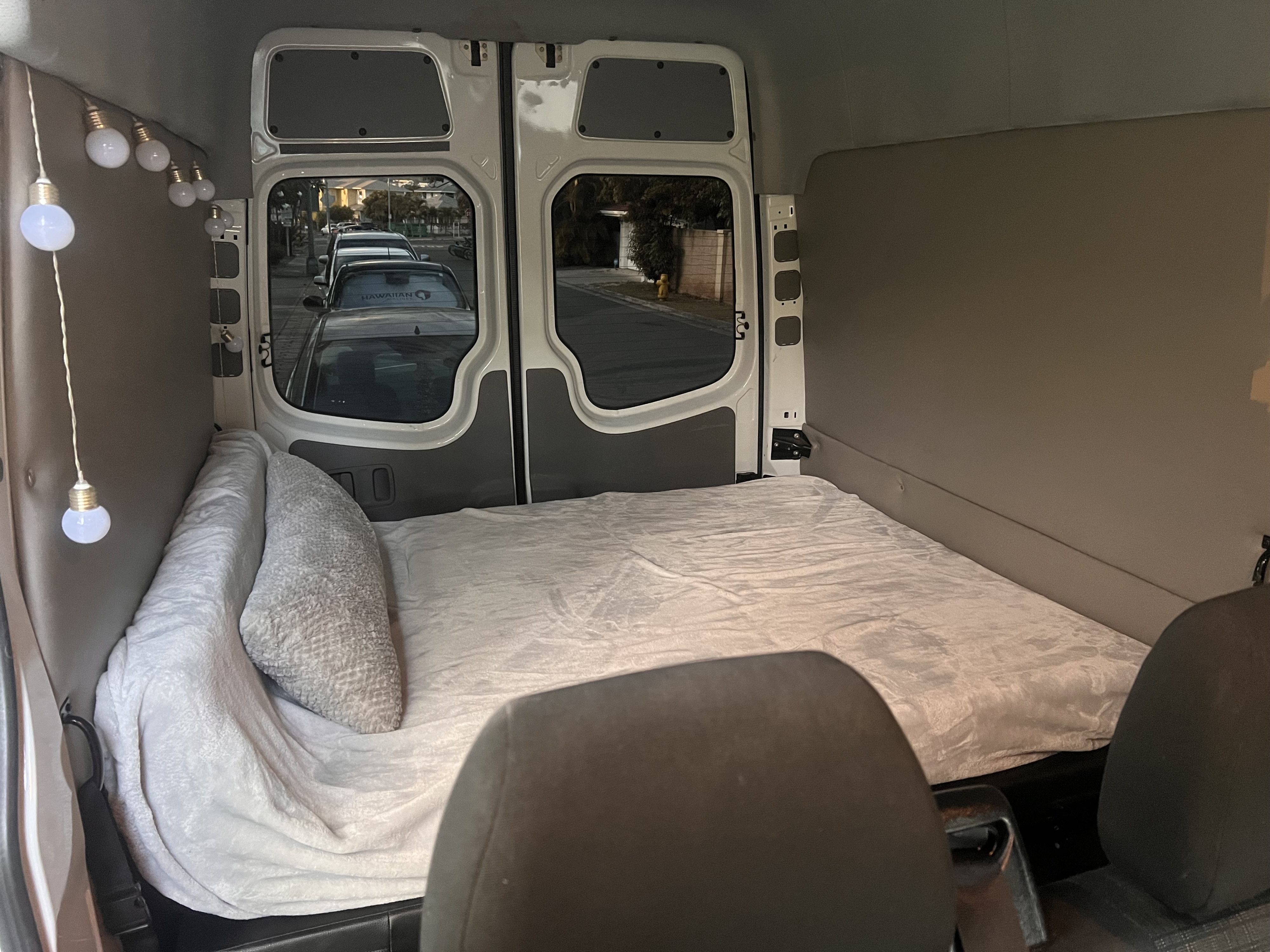 Cozy rv rental van conversion bed setup with string lights and a view from the open rear doors.. Mercedes-Benz Sprinter 2017