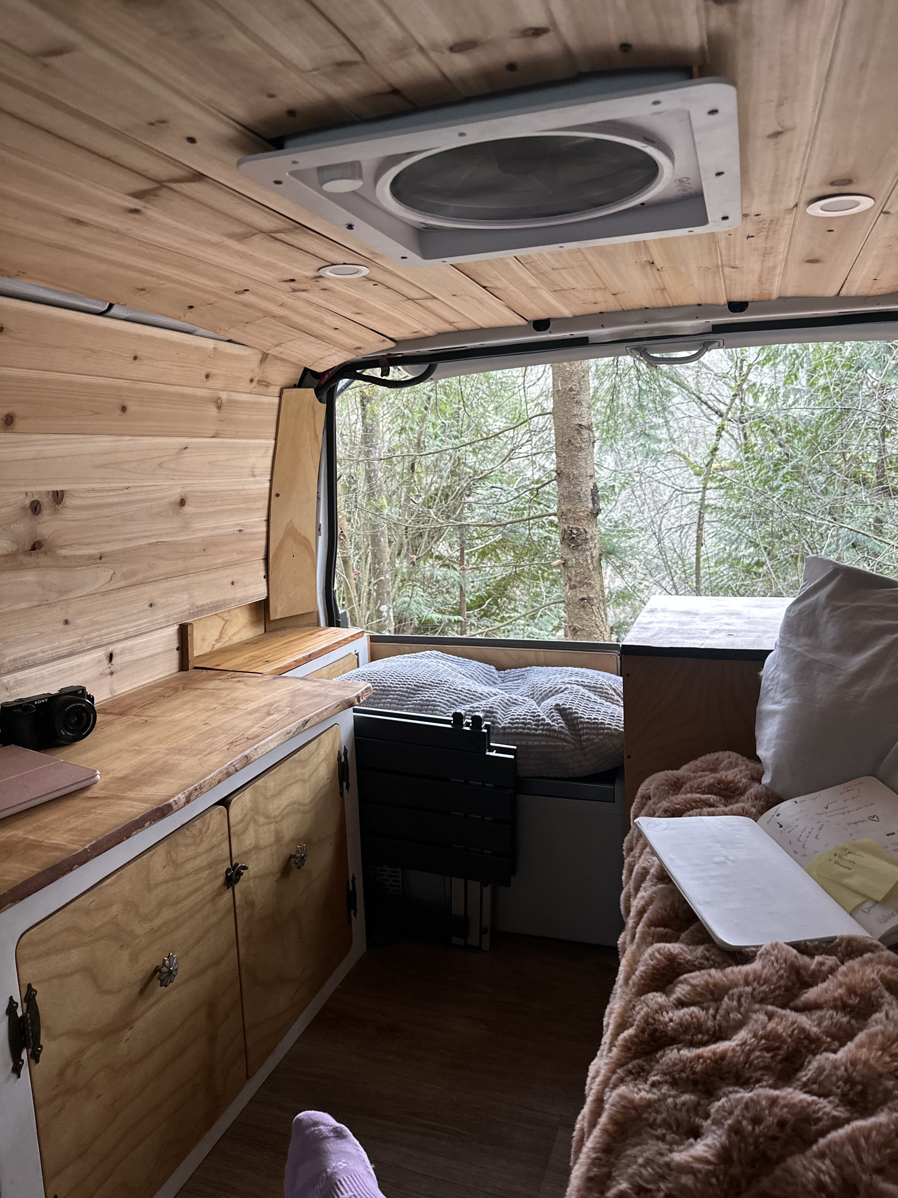 Cozy RV rental interior featuring custom wood, plush bed, work area, and a tranquil forest view. Ideal for travel.. Chevrolet Astro 2003