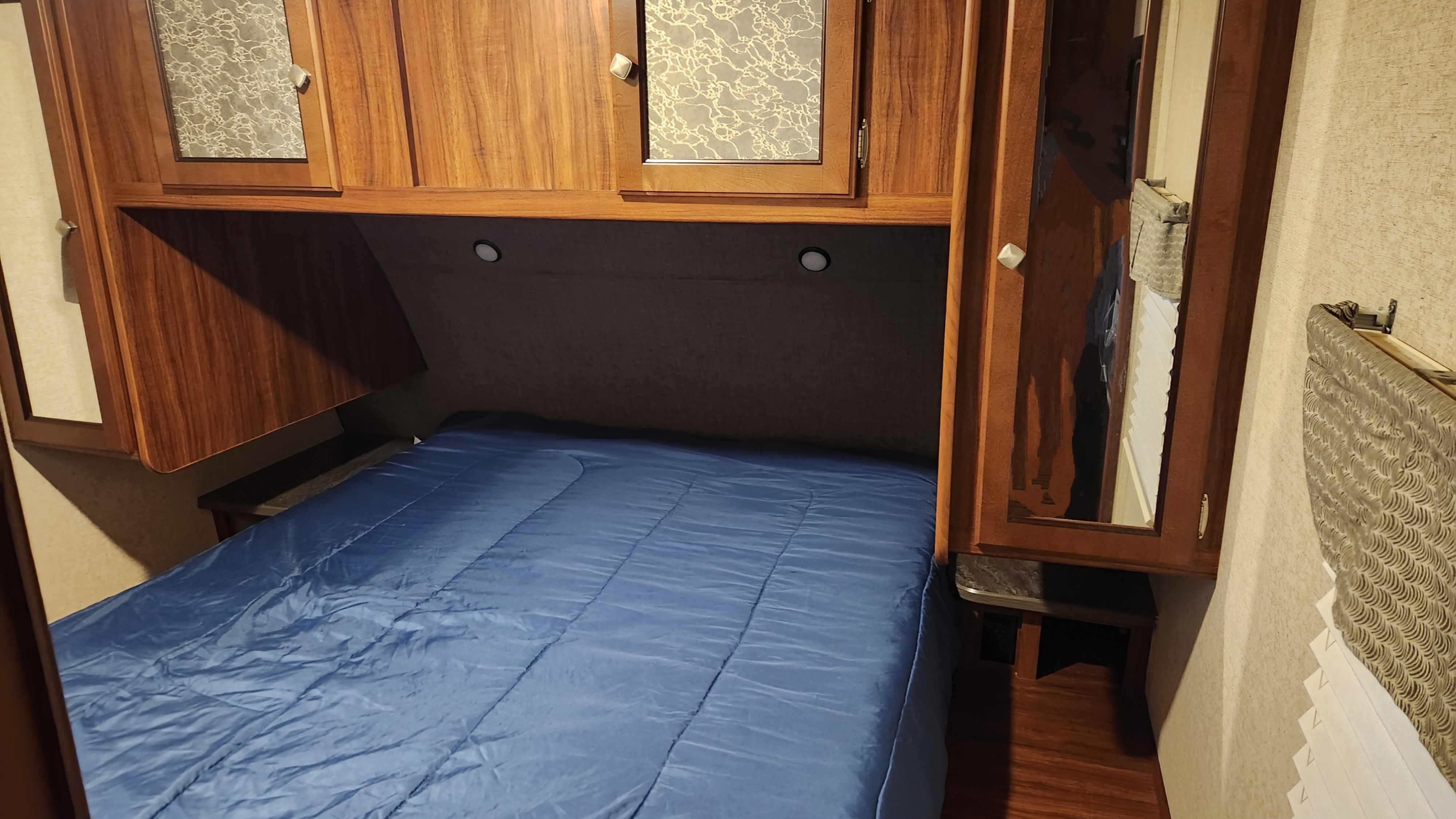 RV rental bedroom with blue bed, wood overhead cabinets, and built-in side tables.. Heartland RVs Mallard 2017