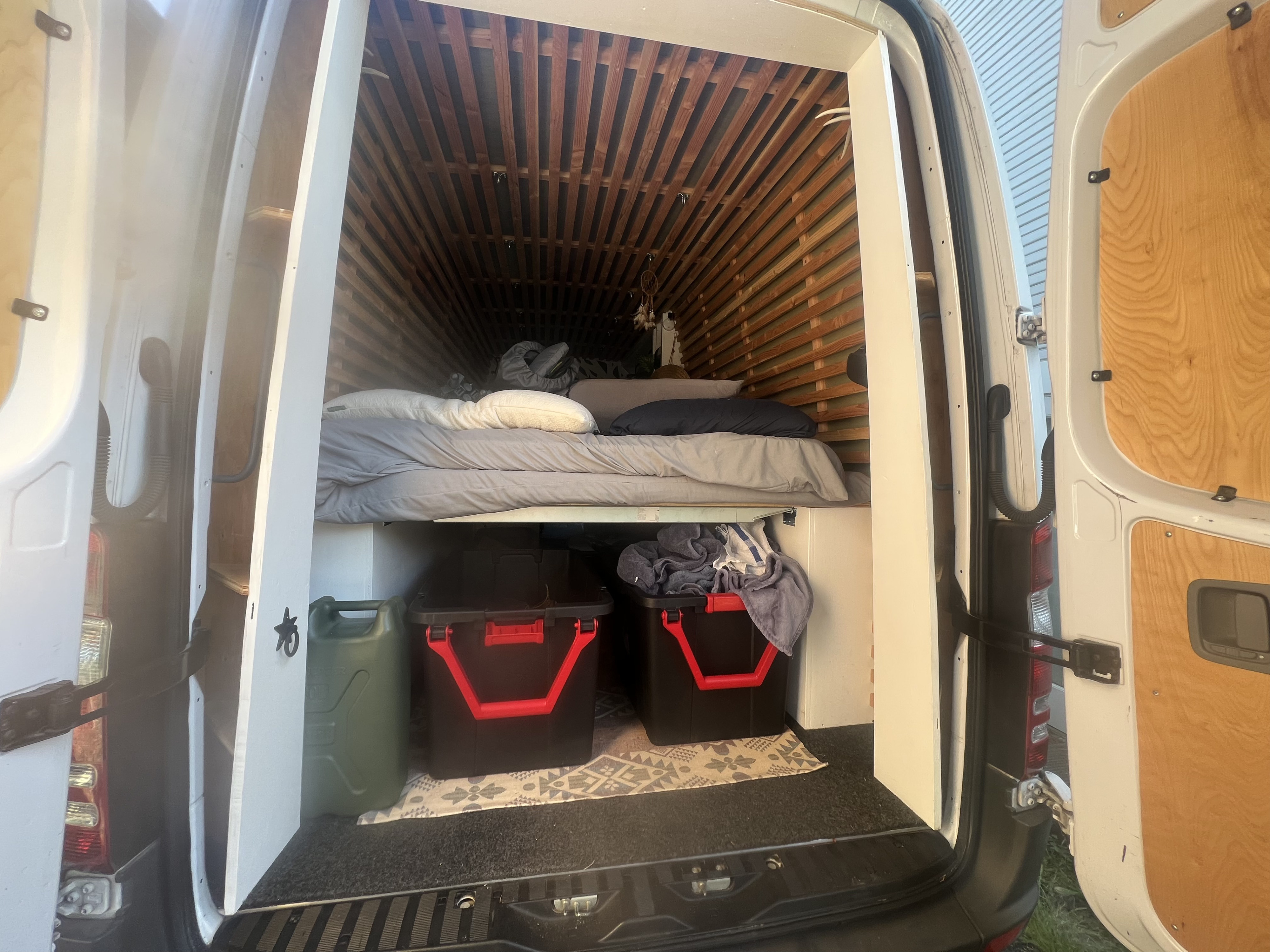 View inside an RV rental's custom camper van conversion, showing a raised bed, wooden slat interior, and organized storage.. Mercedes-Benz sprinter 2017