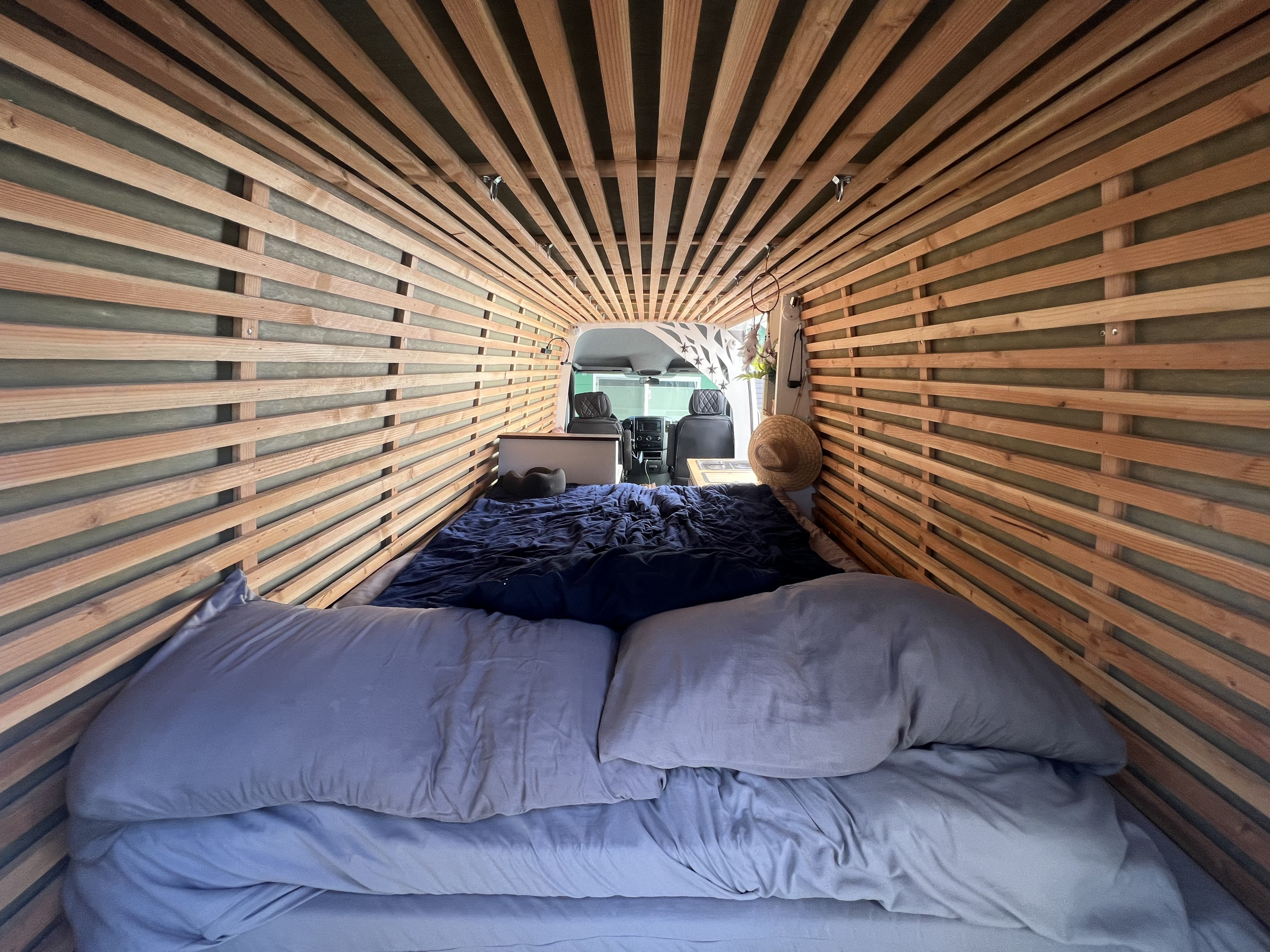 Cozy RV rental interior with custom wood-slatted walls and ceiling, a comfy bed, and a view into the driver's cabin.. Mercedes-Benz sprinter 2017