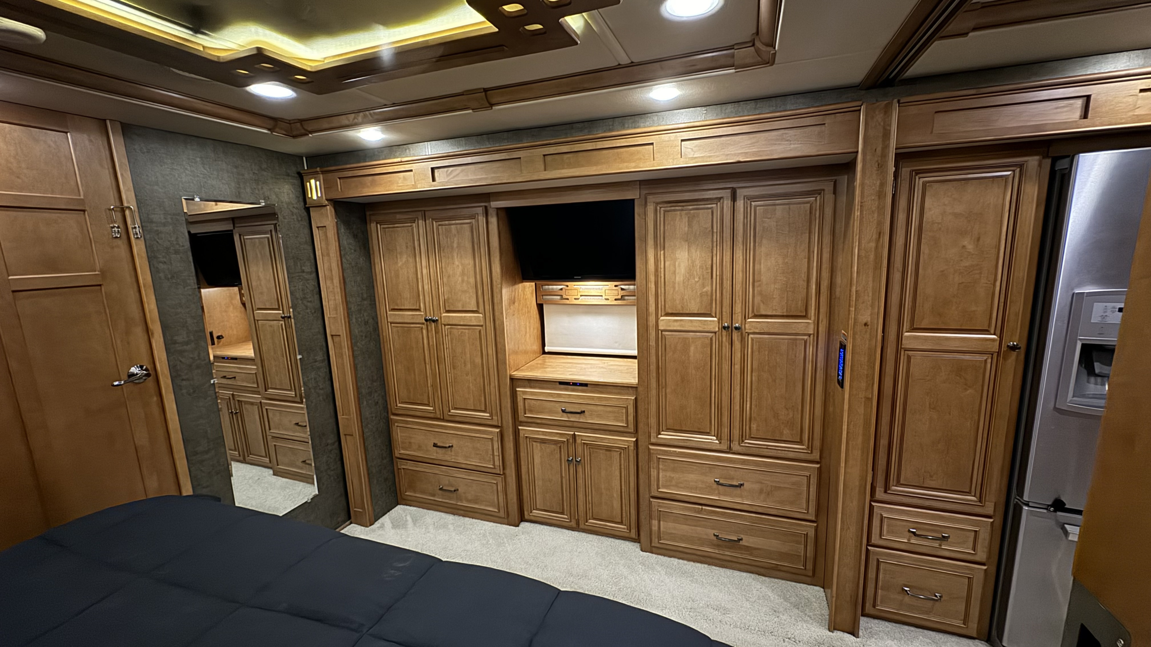 Luxury RV rental interior: rich wood cabinetry, cozy bed, entertainment center, and full-size fridge offer home comforts.. Winnebago Ellipse 2016