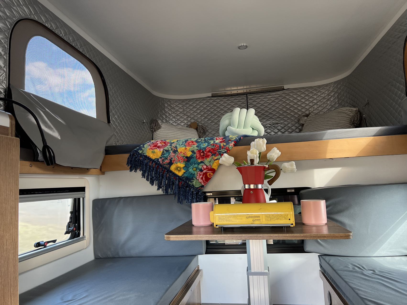 Cozy RV rental interior featuring a bunk bed, dining area with portable stove, coffee pot, & flowers. Window view of sky.. toyota tacoma 2024