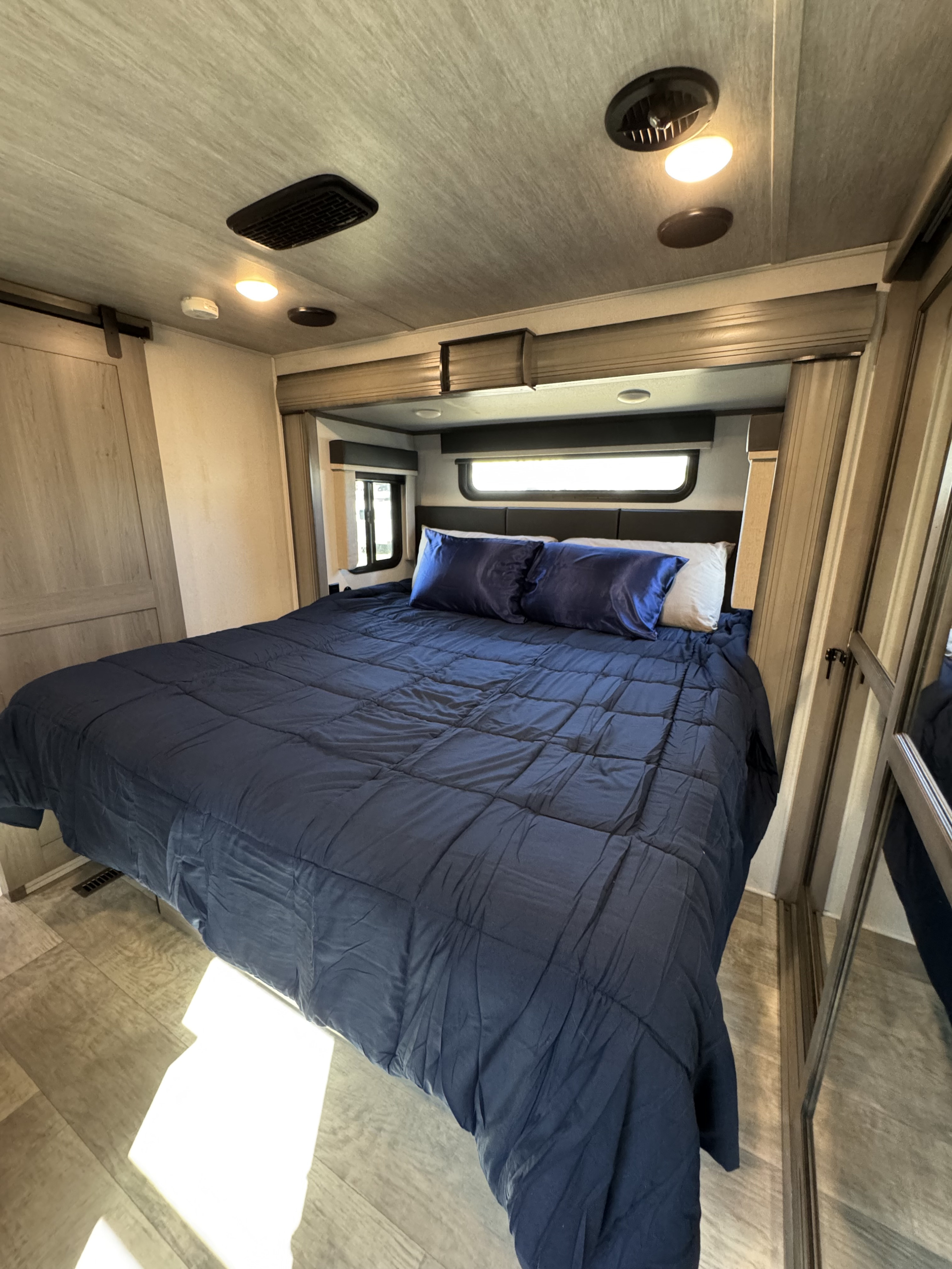 Step into comfort with this spacious RV rental bedroom featuring a queen bed with blue bedding, ample storage, and natural light.. Keystone RV Montana 2020