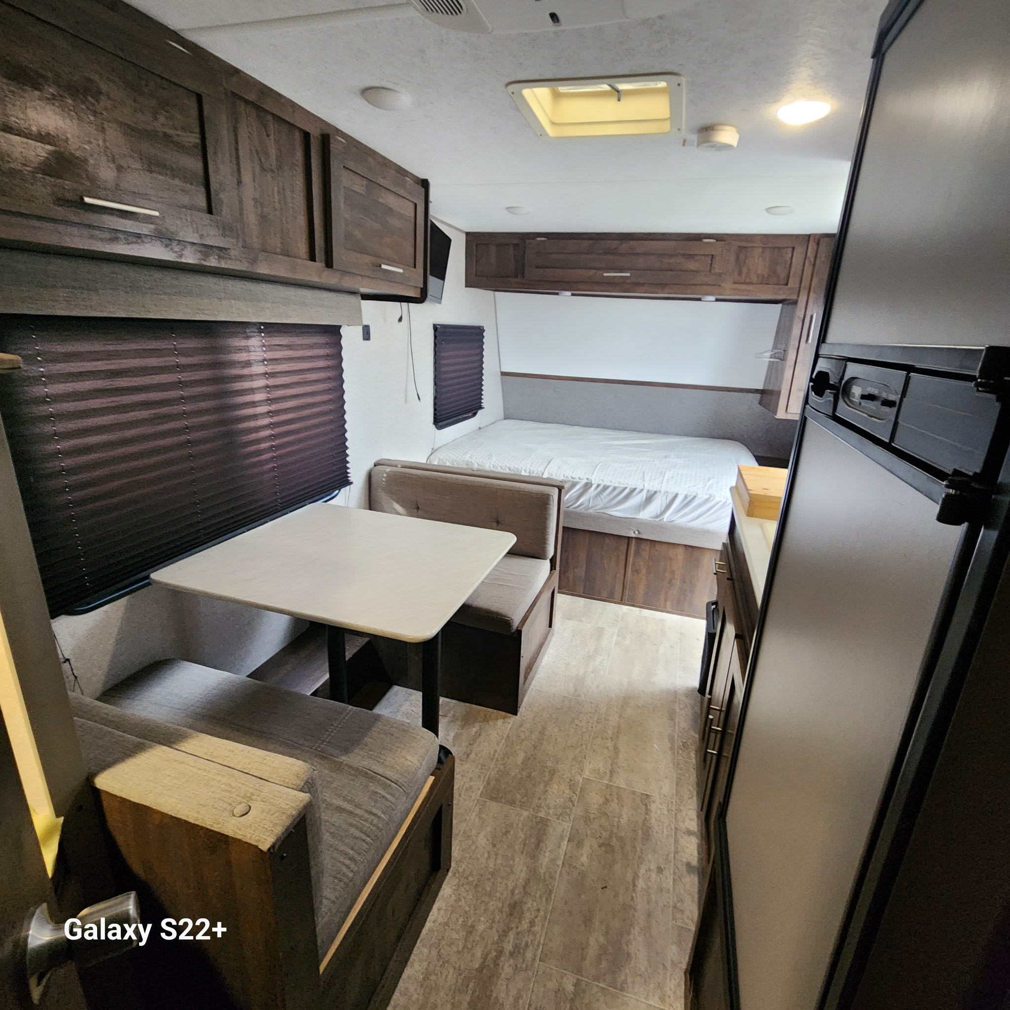 An RV rental interior with a cozy dinette, sleeping area, and compact kitchen featuring dark wood cabinets and light flooring.. Ozark Lite 2020