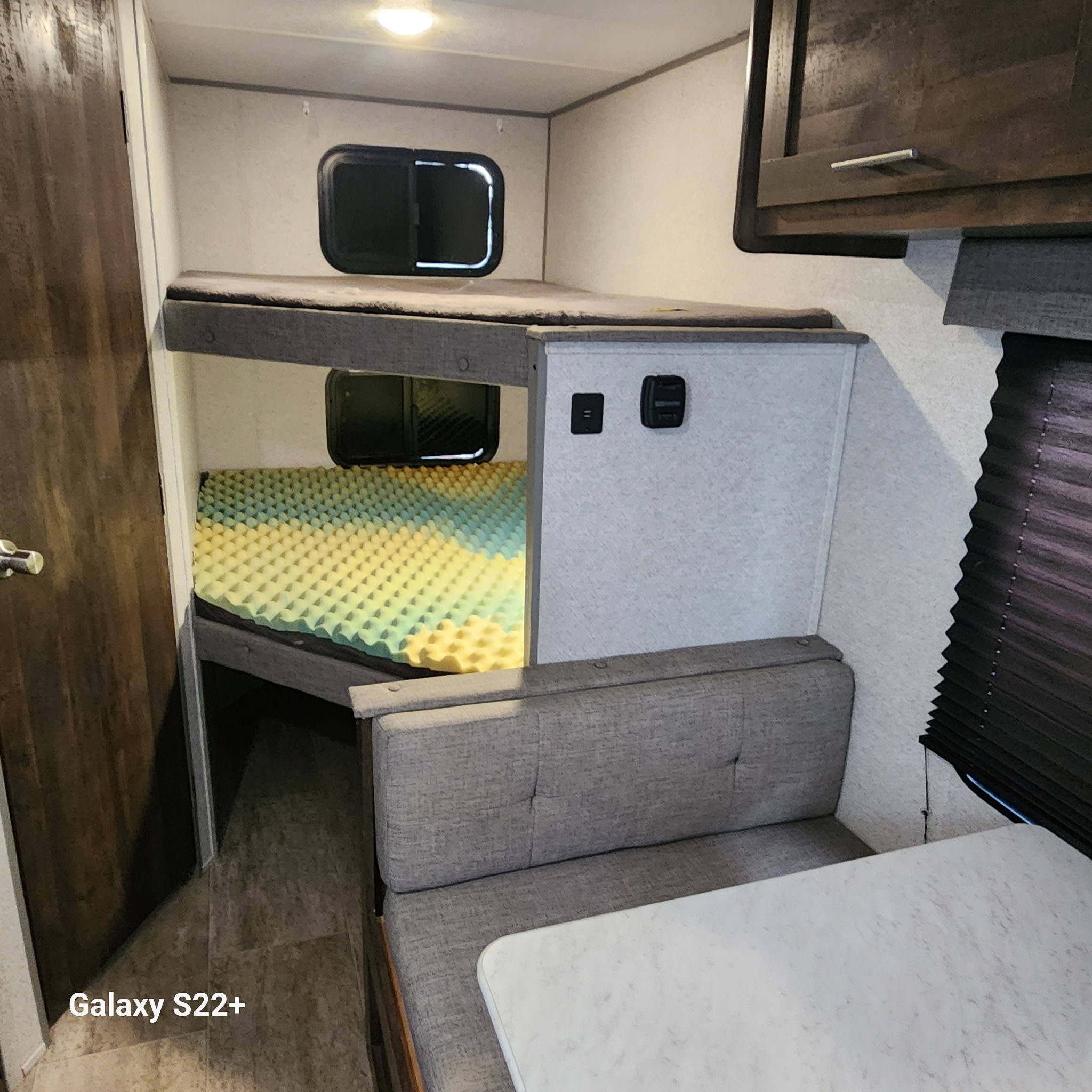RV rental interior showcasing bunk beds with a distinctive yellow/green foam mattress, a dinette, and overhead storage.. Ozark Lite 2020
