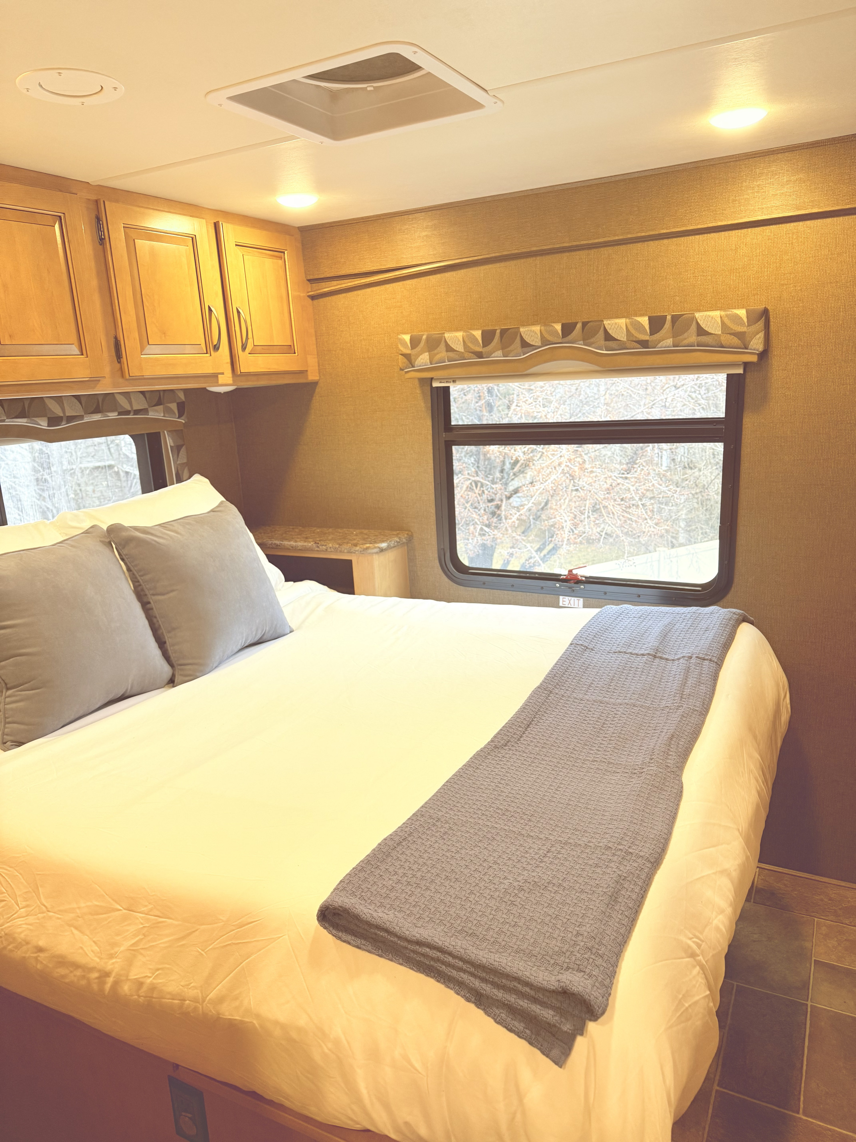Cozy rv rental bedroom with a comfortable bed, wooden cabinets, and a window offering a view of bare trees.. Thor Chateau 2017