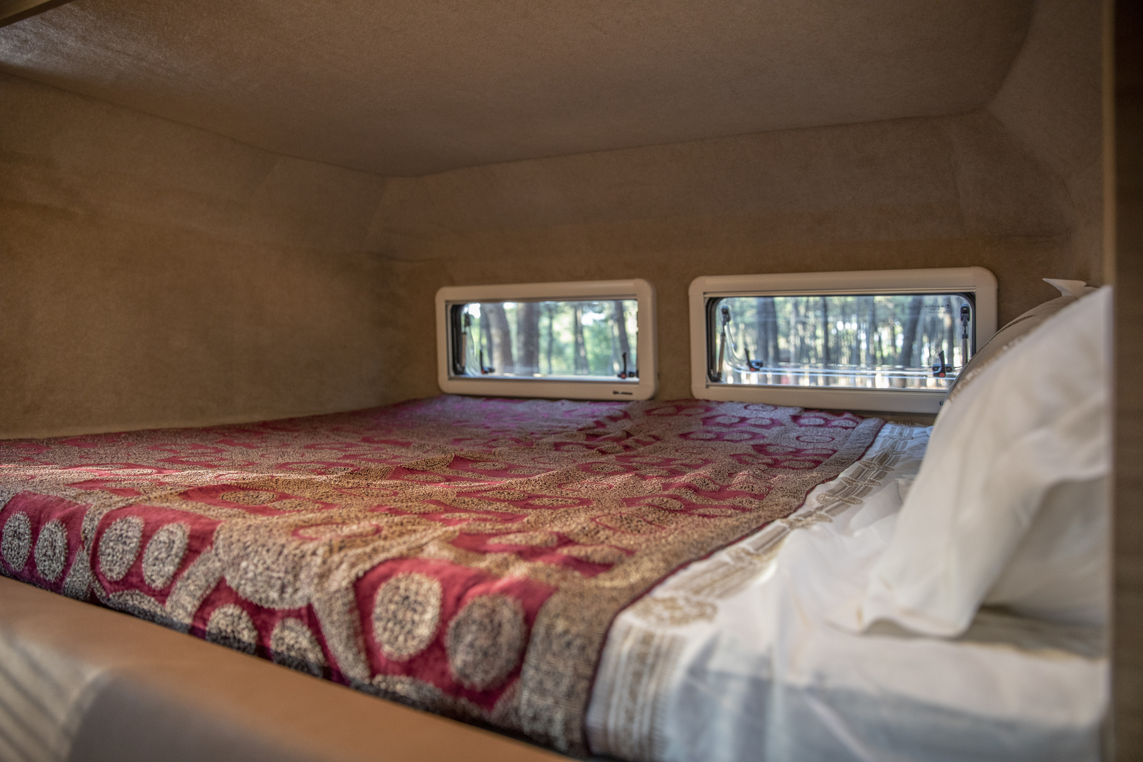RV rental: A comfy bed with a red blanket and dual windows showcasing peaceful forest views inside this cozy space.. Ford F-150 Gas / Propane Hybrid and Hotomobil Gladiator XL Extended with roof tent 2020