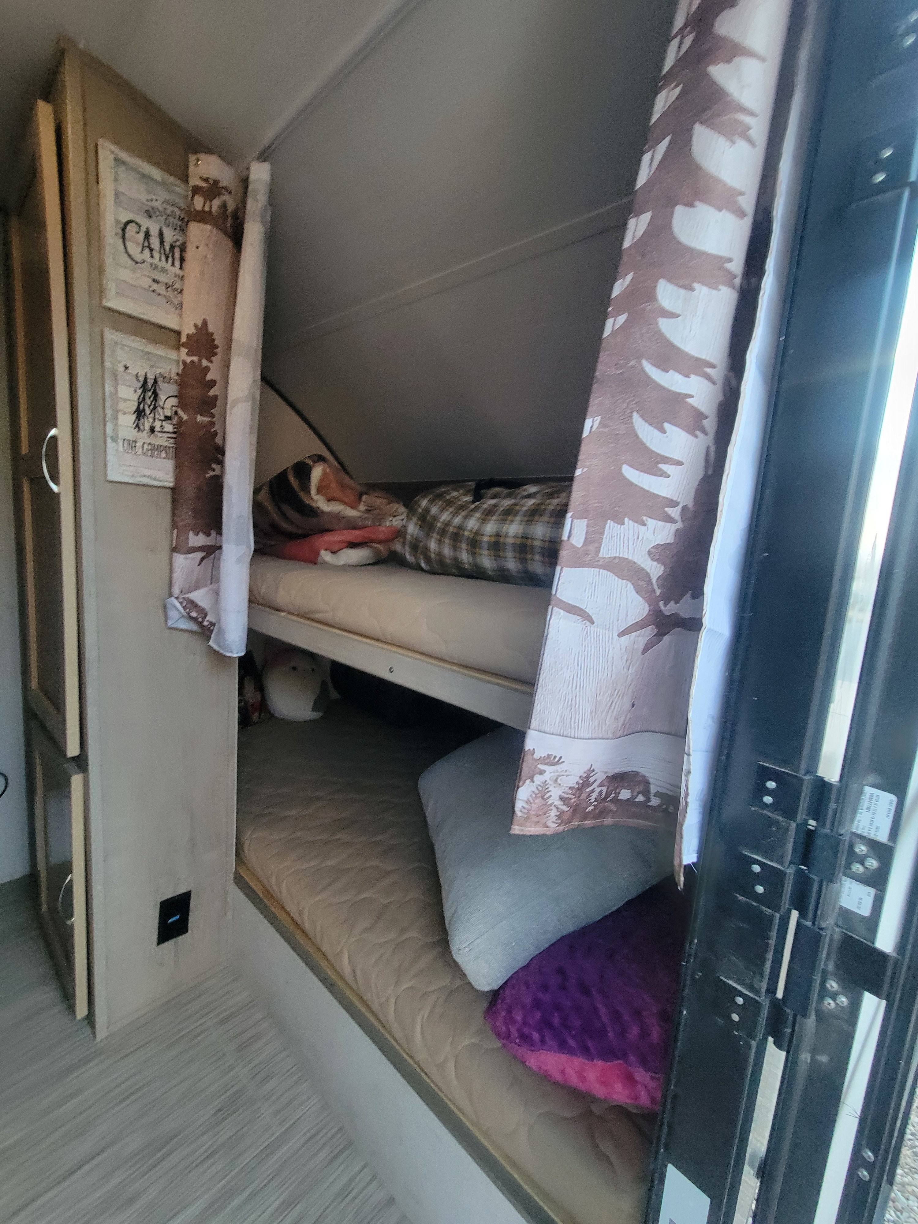 An RV rental's cozy bunk bed area features patterned curtains and cabin-themed decor. A person rests on the top bunk.. Forest River RPT-176 47 2018
