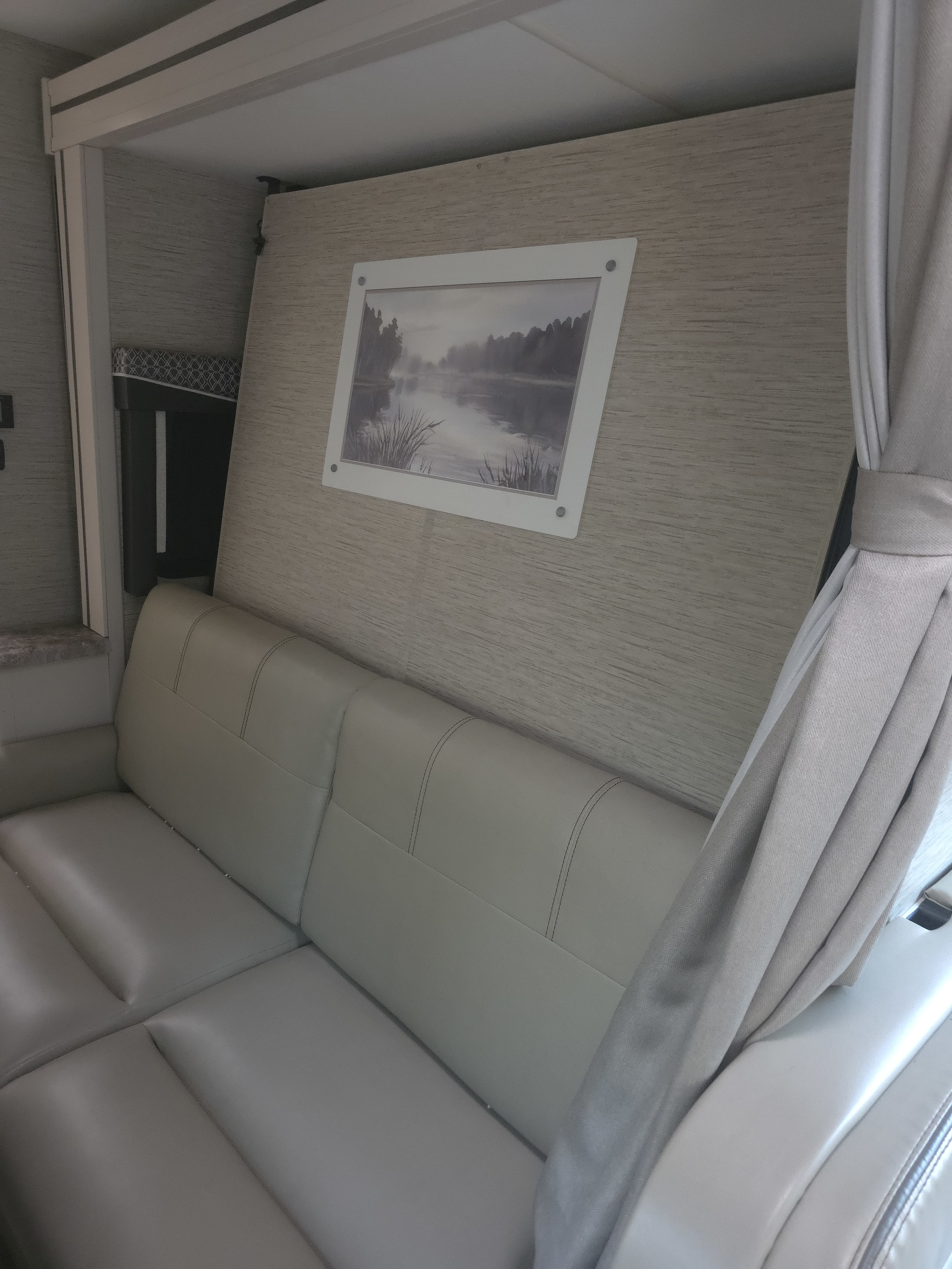 RV rental interior: comfy light-colored sofa, wall art depicting a misty lake, and soft curtains for privacy.. Thor Four Winds 2023