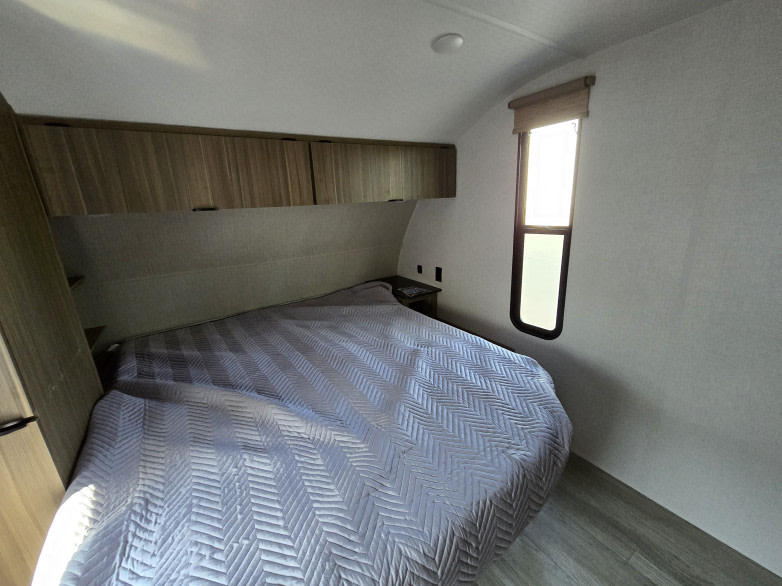 This RV rental features a cozy bedroom with a large bed, overhead cabinets, and a side window, providing a comfortable sleeping area.. Forest River Salem Cruise Lite 2025