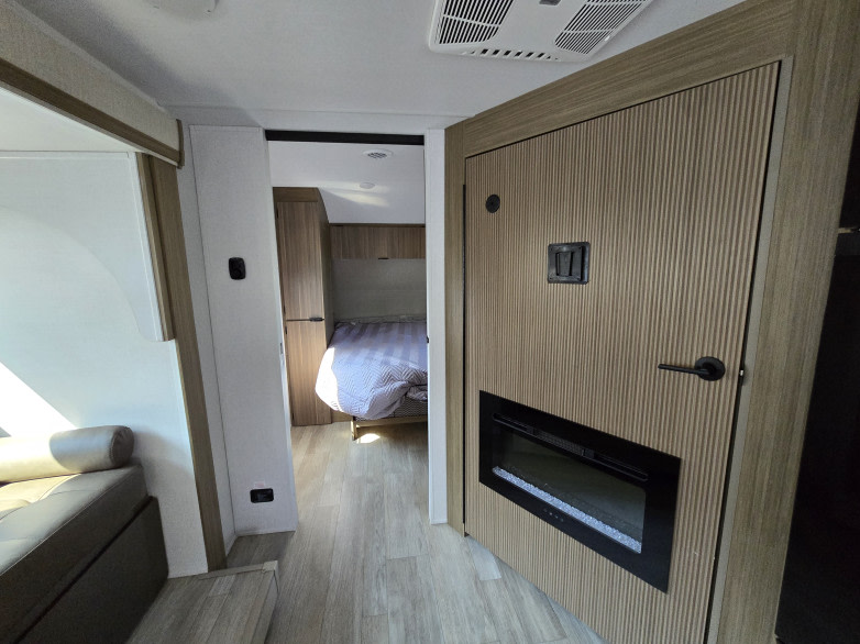 View of a modern RV rental interior showing the living area, a hallway to the bedroom, and a wall with a built-in electric fireplace.. Forest River Salem Cruise Lite 2025