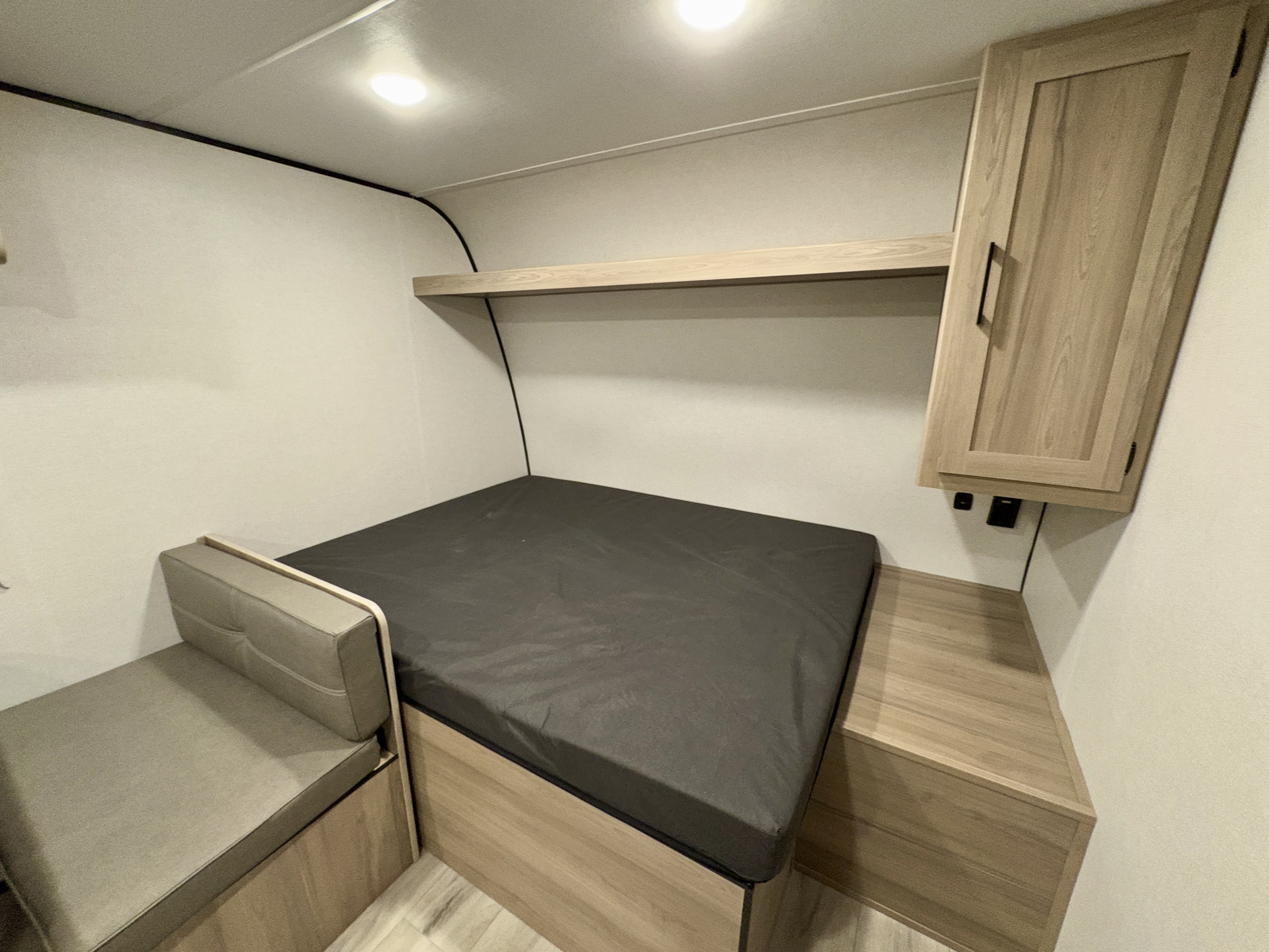 Modern RV rental bedroom with a bed, dinette, overhead shelf, wall cabinet, and ceiling lights, ideal for comfortable travel.. Coleman Keystone Light 17BX 2025