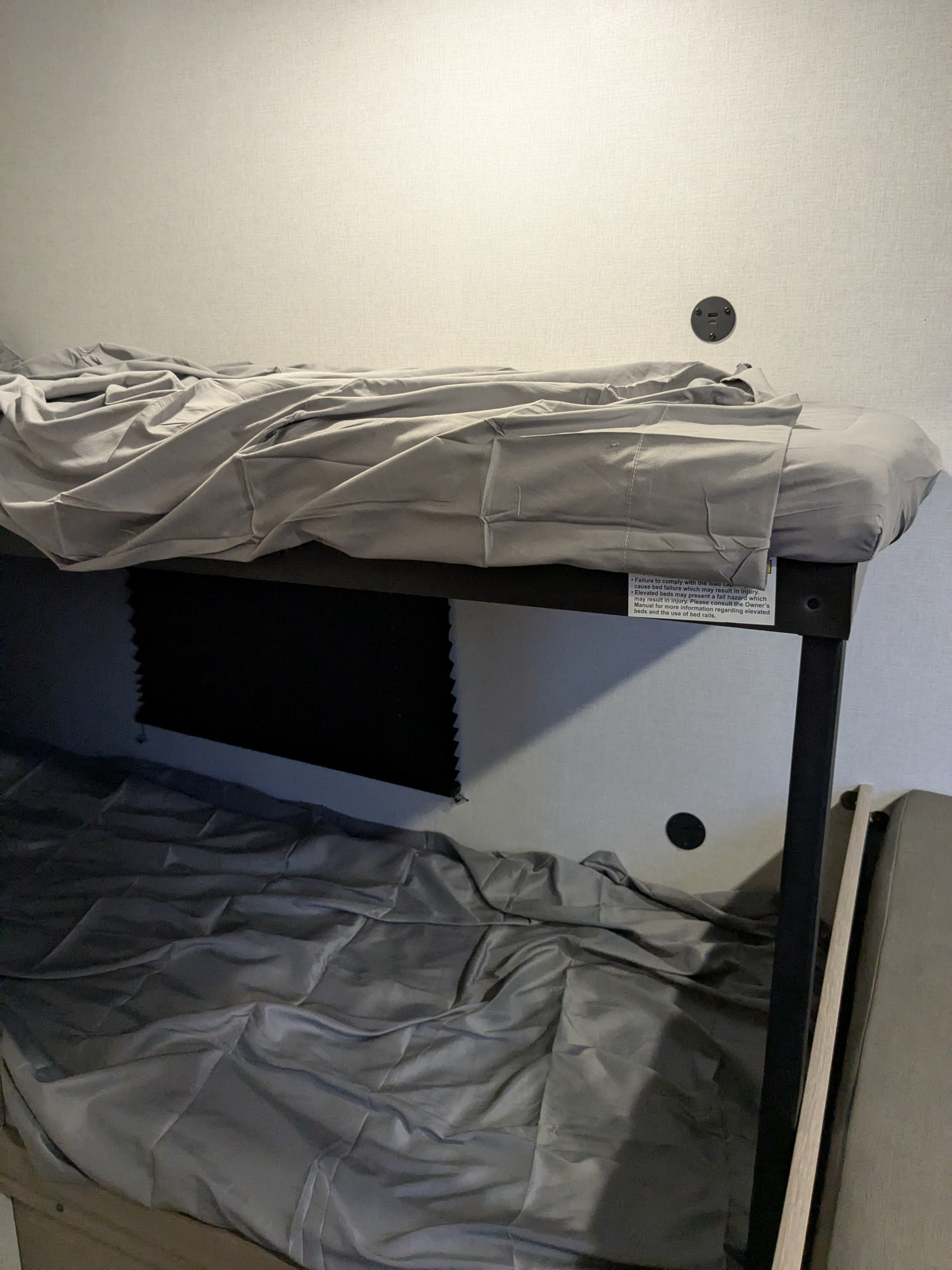 Cozy RV rental bunk beds with grey sheets, a visible safety warning, and convenient USB charging ports for travelers.. Keystone Coleman 2025