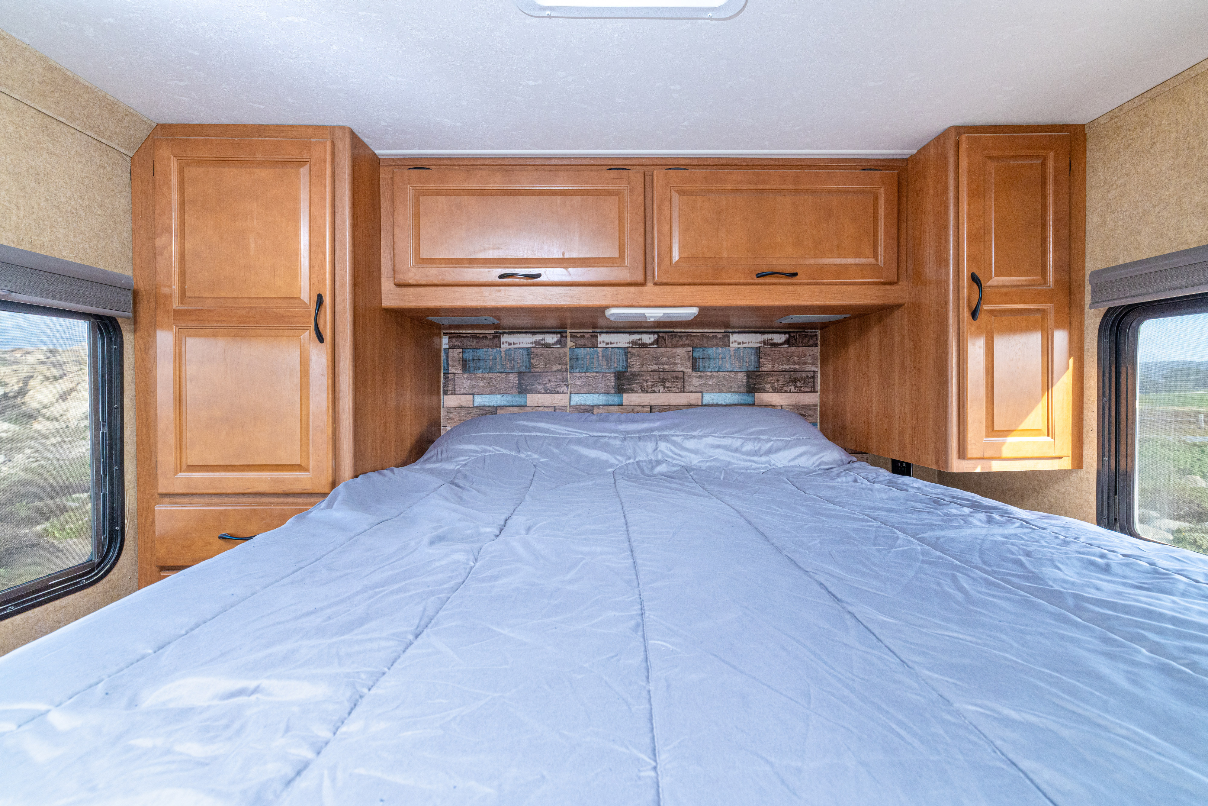 RV rental bedroom: cozy bed, wood cabinets, decorative headboard, and window views for a comfortable stay.. Thor Motor Coach Four Winds Majestic 2015