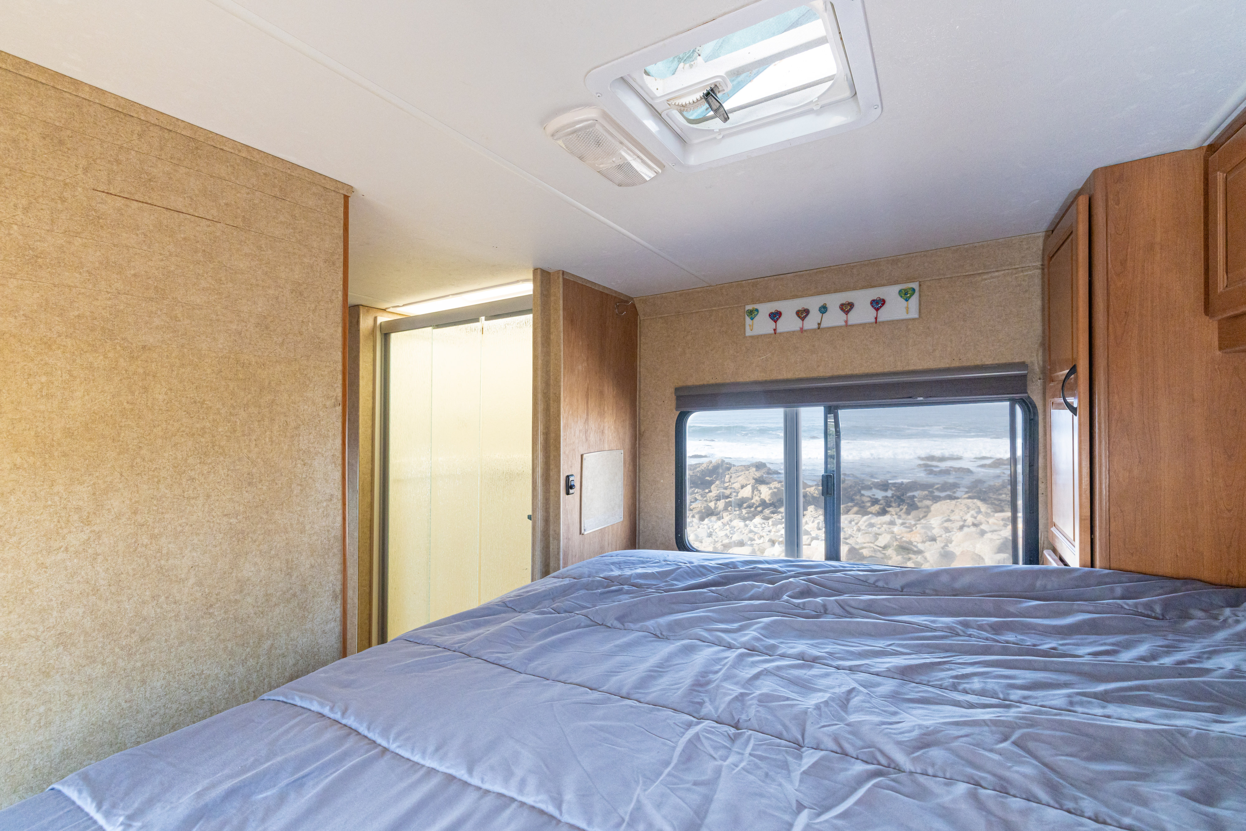 RV rental bedroom with a cozy bed, en-suite shower, and stunning ocean view overlooking a rocky coastline.. Thor Motor Coach Four Winds Majestic 2015