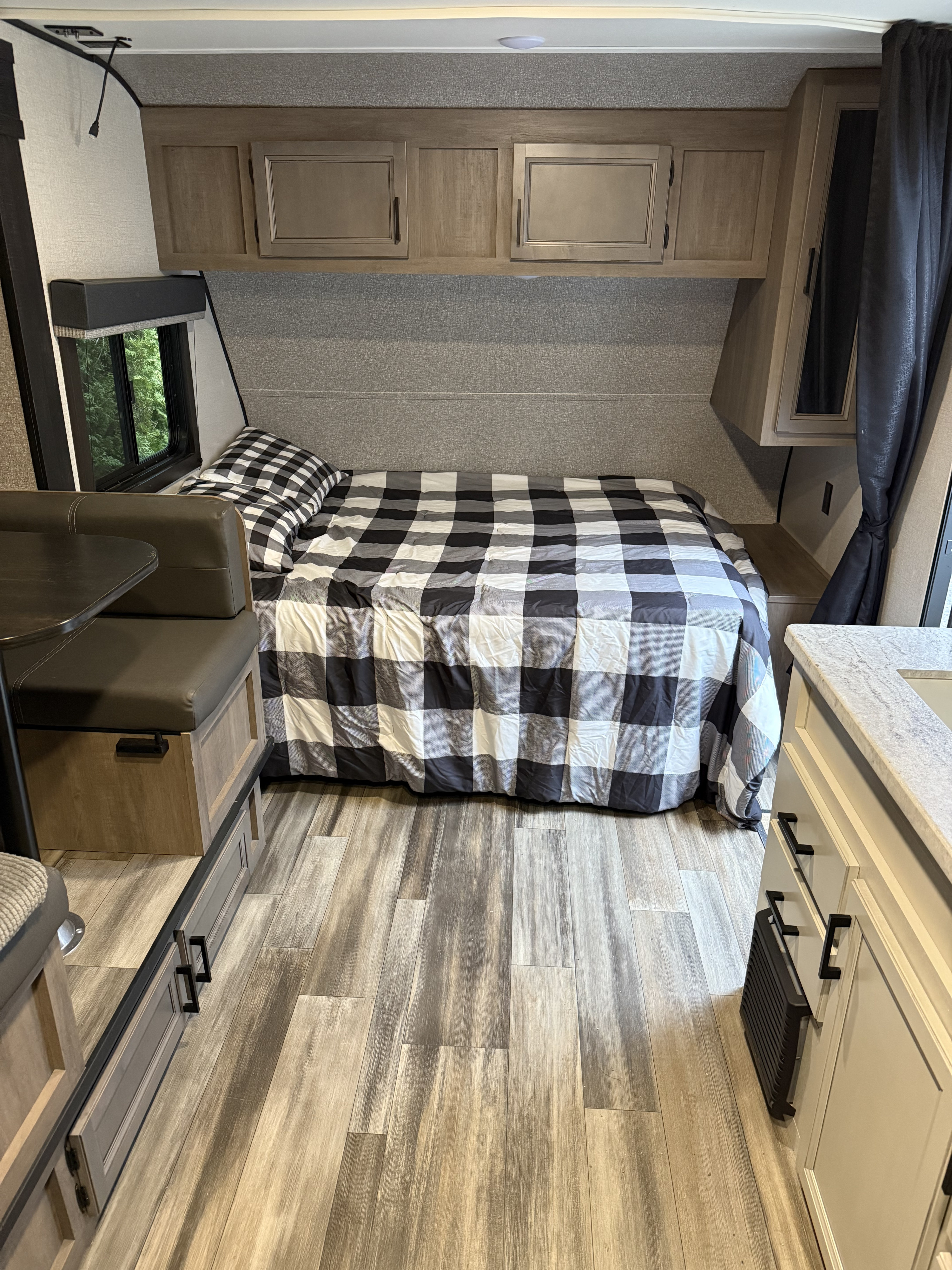 RV rental interior with a black & white plaid bed, overhead cabinets, dinette, and wood-look flooring.. Highland Ridge RV Open Range 2022