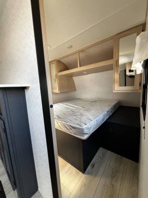 Explore this RV rental bedroom: a bed with overhead cabinets & wood floors, ready for your adventure.. Avenger 28QBSLE 2025