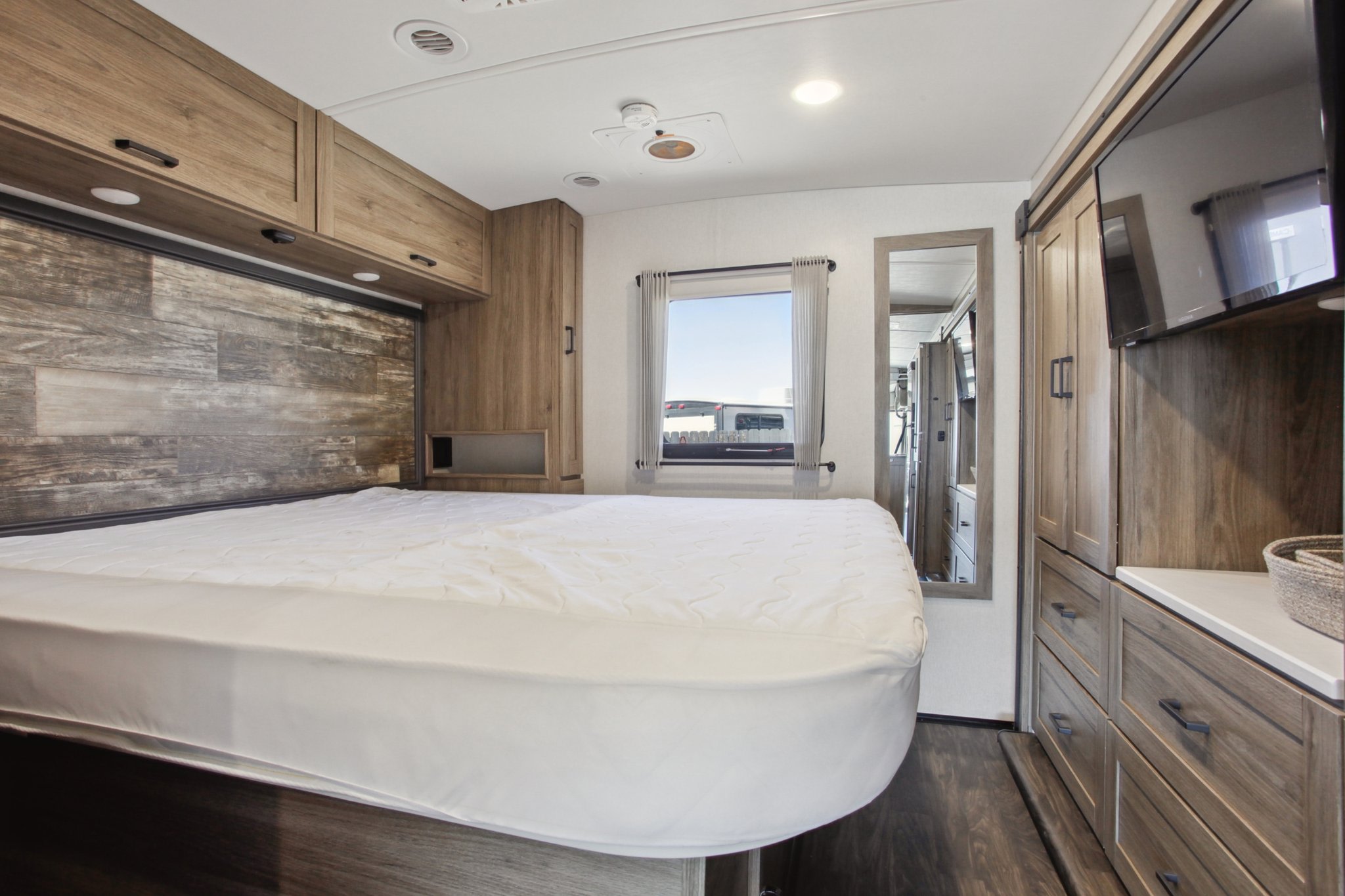 RV rental bedroom with a large bed, warm wood interior, TV, and ample storage, ready for your next adventure.. Winnebago Vista 2023