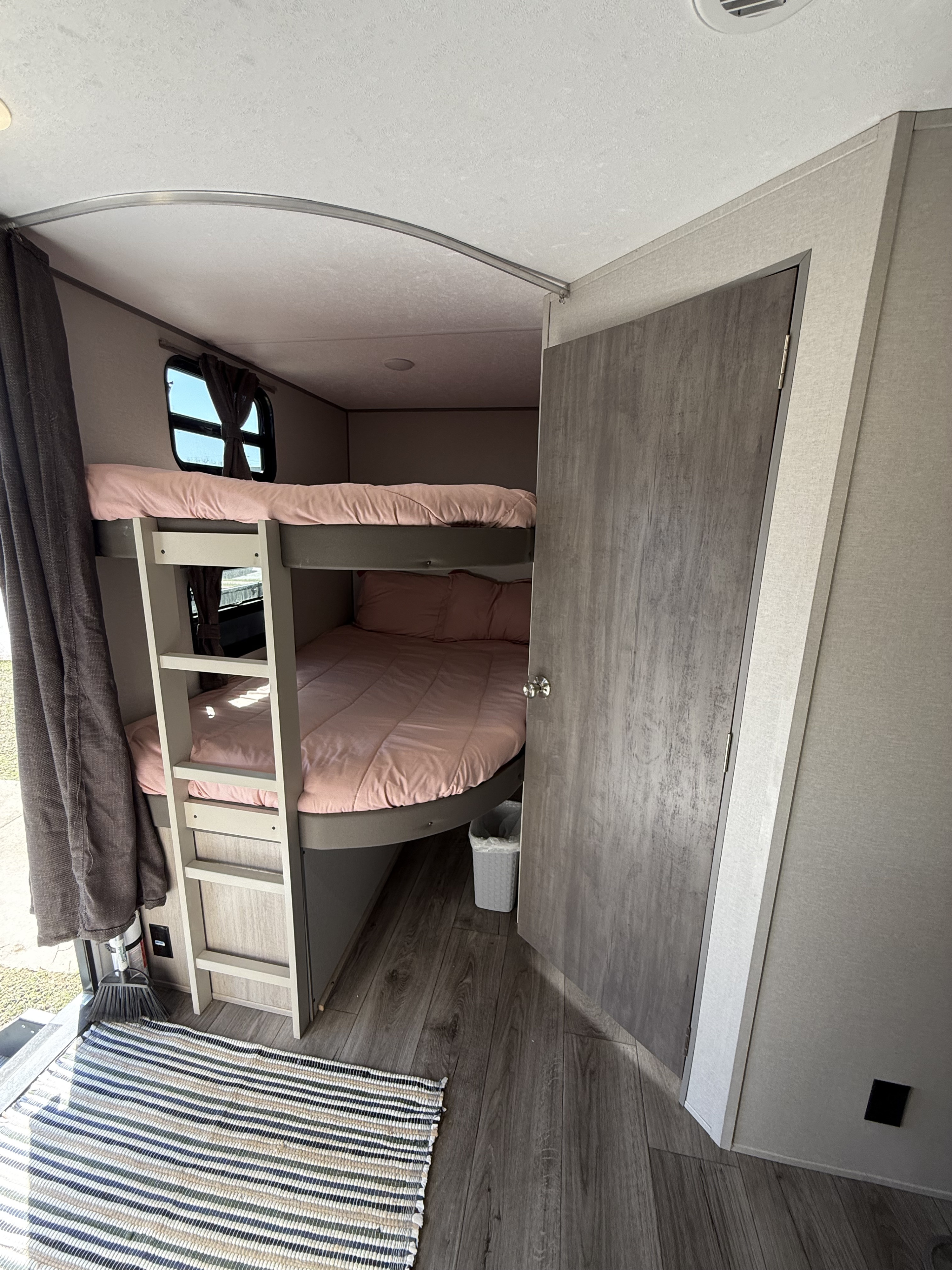Inside an RV rental: a cozy bunk bed area with pink bedding, small windows, and a ladder. Perfect for family adventures.. Coachmen Catalina 2024