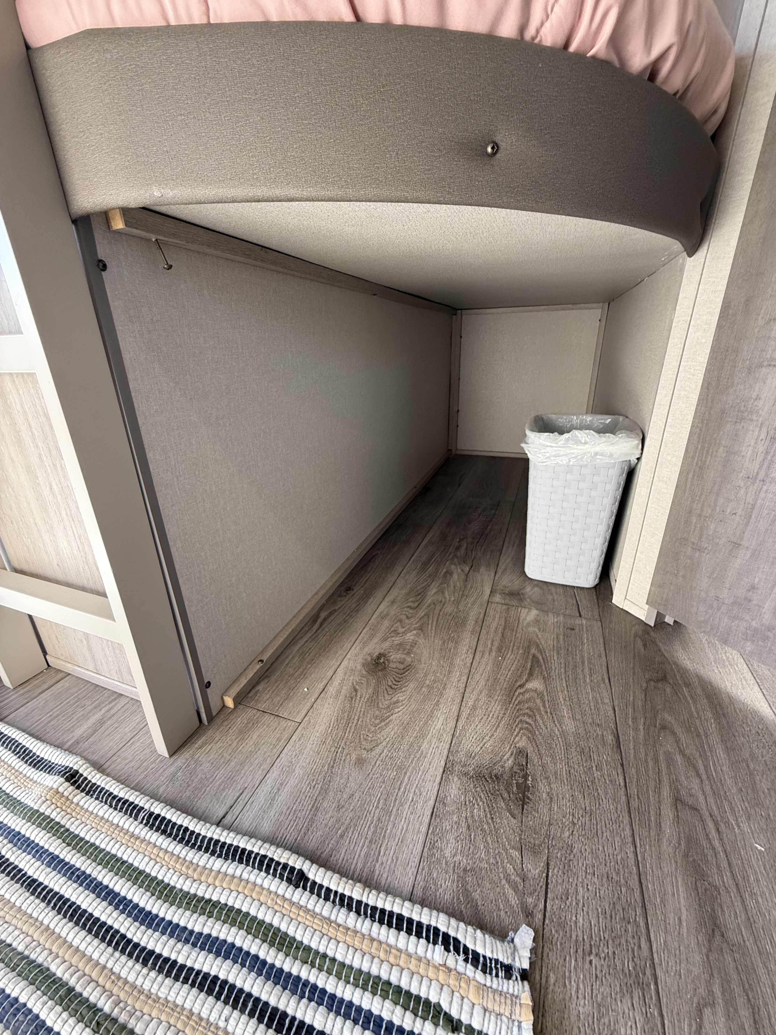 RV rental's under-bunk storage, showing wood-look floor, a striped rug, and a white wastebasket.. Coachmen Catalina 2024