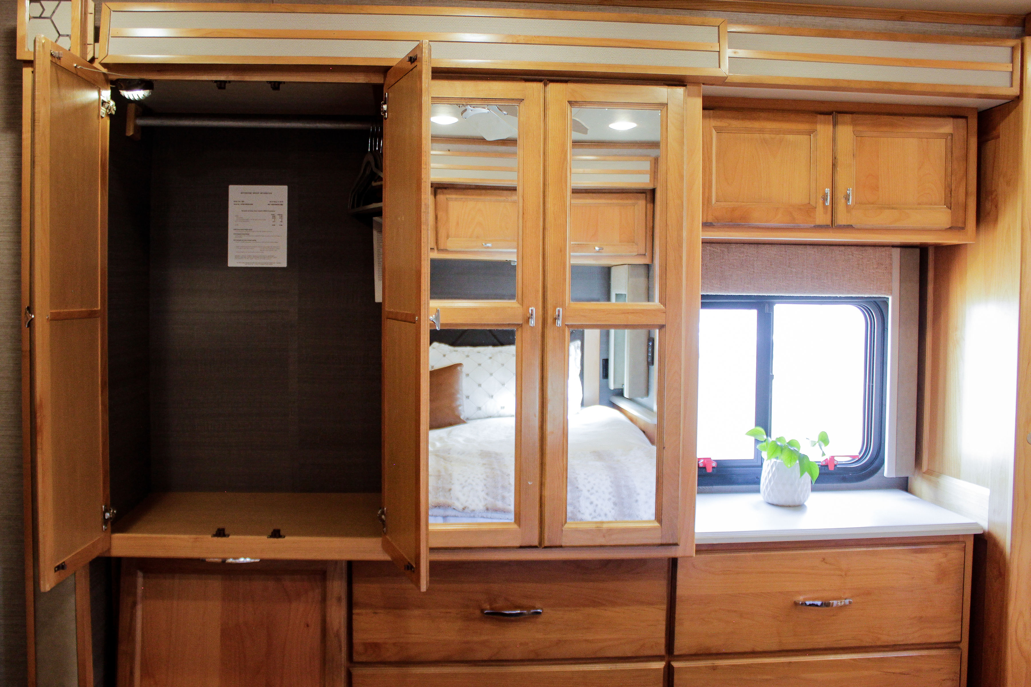 RV rental interior: bedroom area with open closet, mirrored cabinets reflecting the bed, wooden drawers, and large window.. Allegro Allegro Open Road 2021