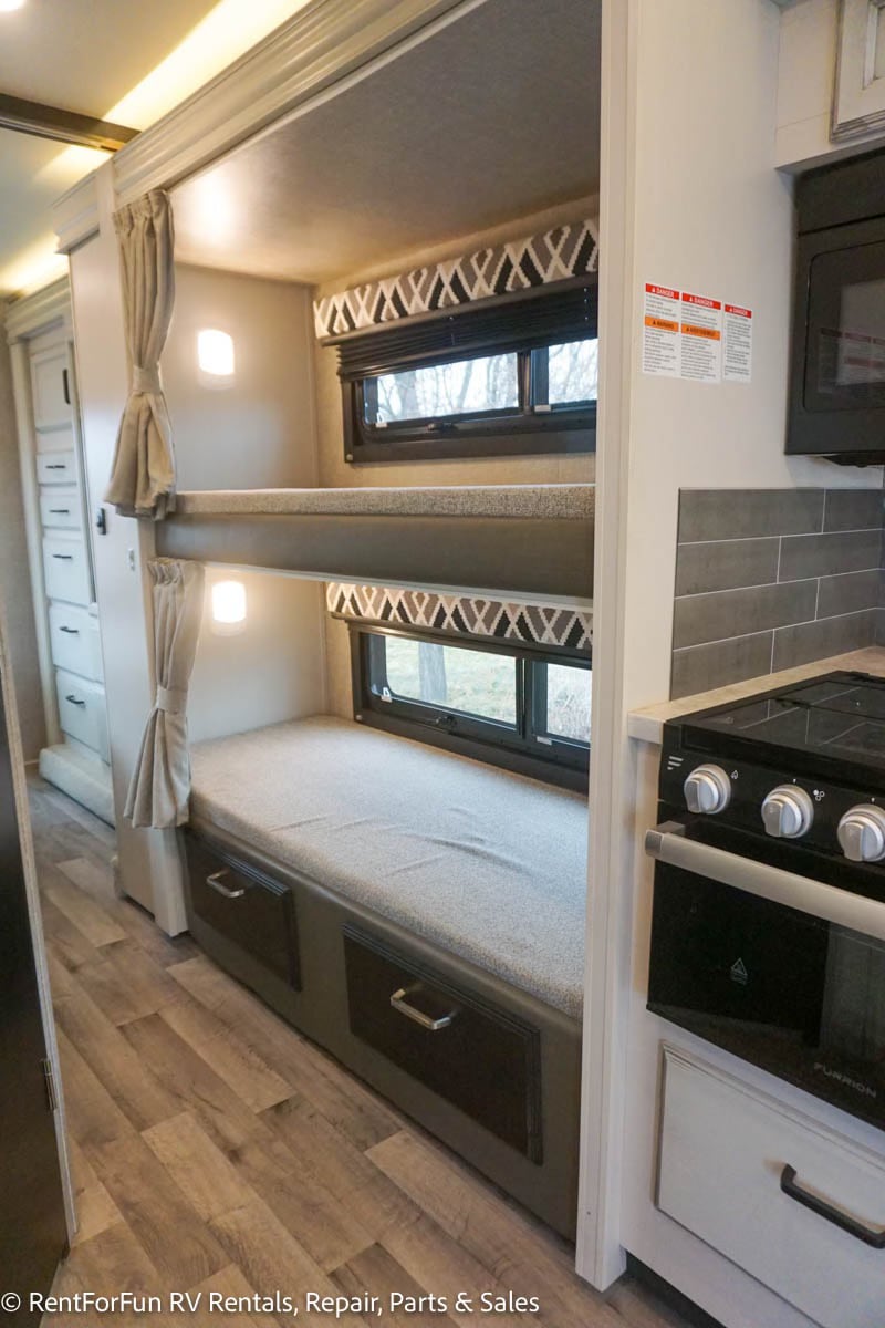 Inside this RV rental, find cozy bunk beds with windows, built-in storage, and a compact kitchen area.. Jayco Redhawk 2022