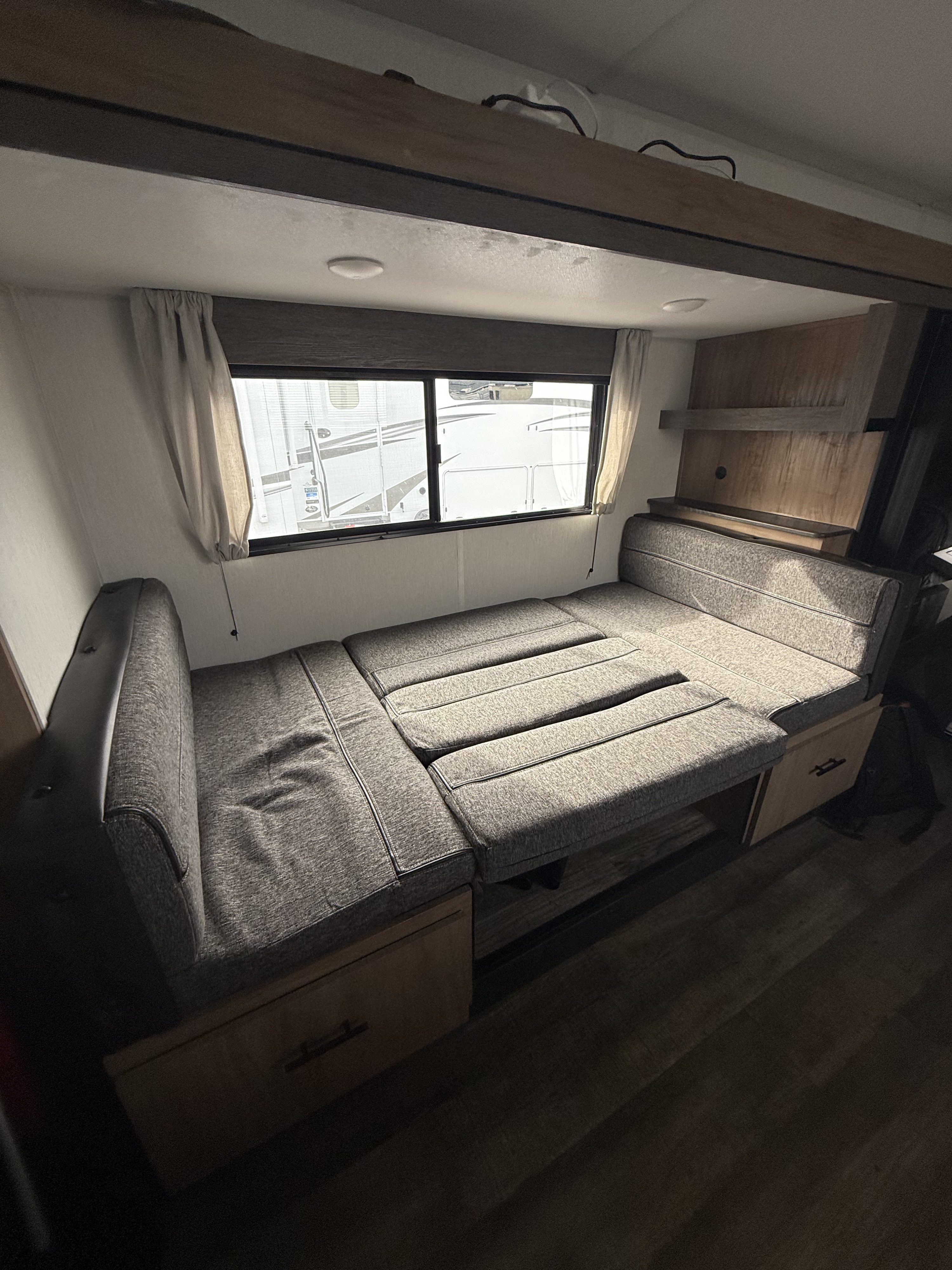 Cozy RV rental interior showcasing a versatile grey sofa that converts into a bed, featuring storage drawers and windows.. Forest River Campsite Reserve 23CC 2024