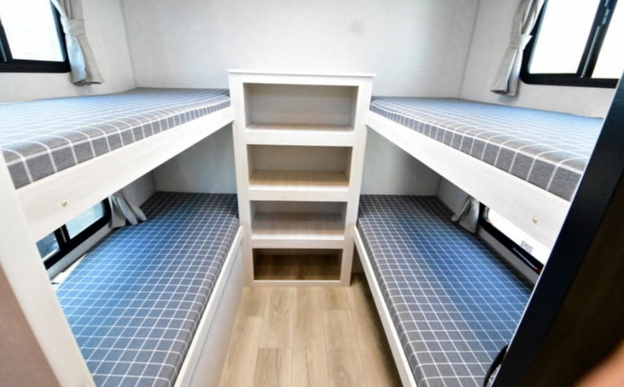 Inside an RV rental: a cozy bunkhouse with four beds, complete with checkered mattresses and a central storage unit.. Forest river Surveyor legend x 2025