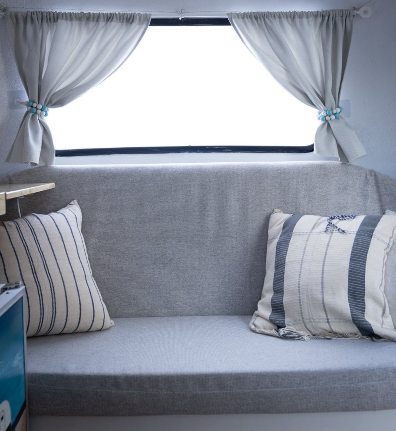 Cozy RV rental interior with grey seating, striped pillows, and bright window curtains.. Boler Boler 1974