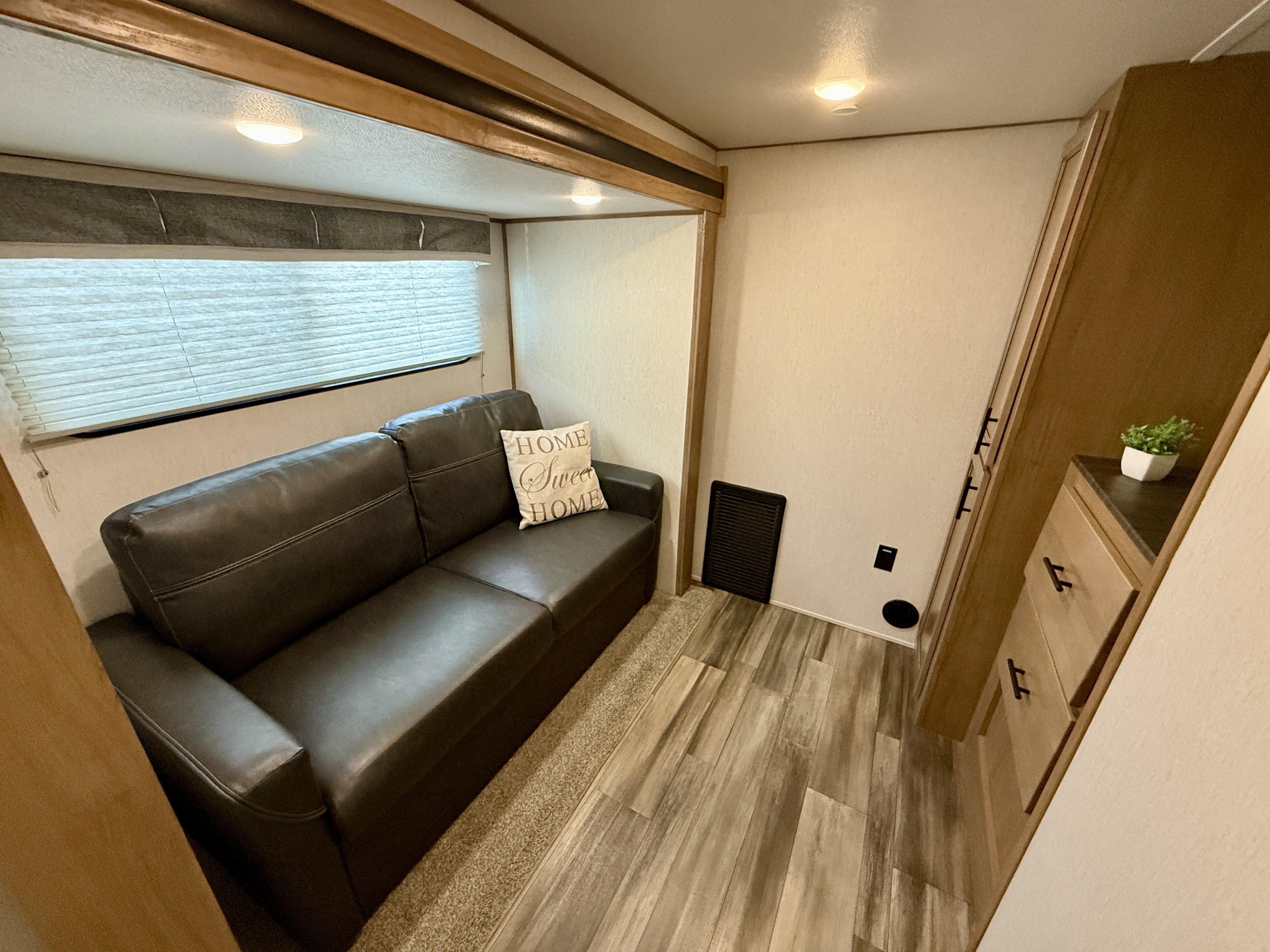 Cozy RV rental interior featuring a comfortable sofa, window blinds, and practical storage with a small plant.. Forest River Sabre 2023