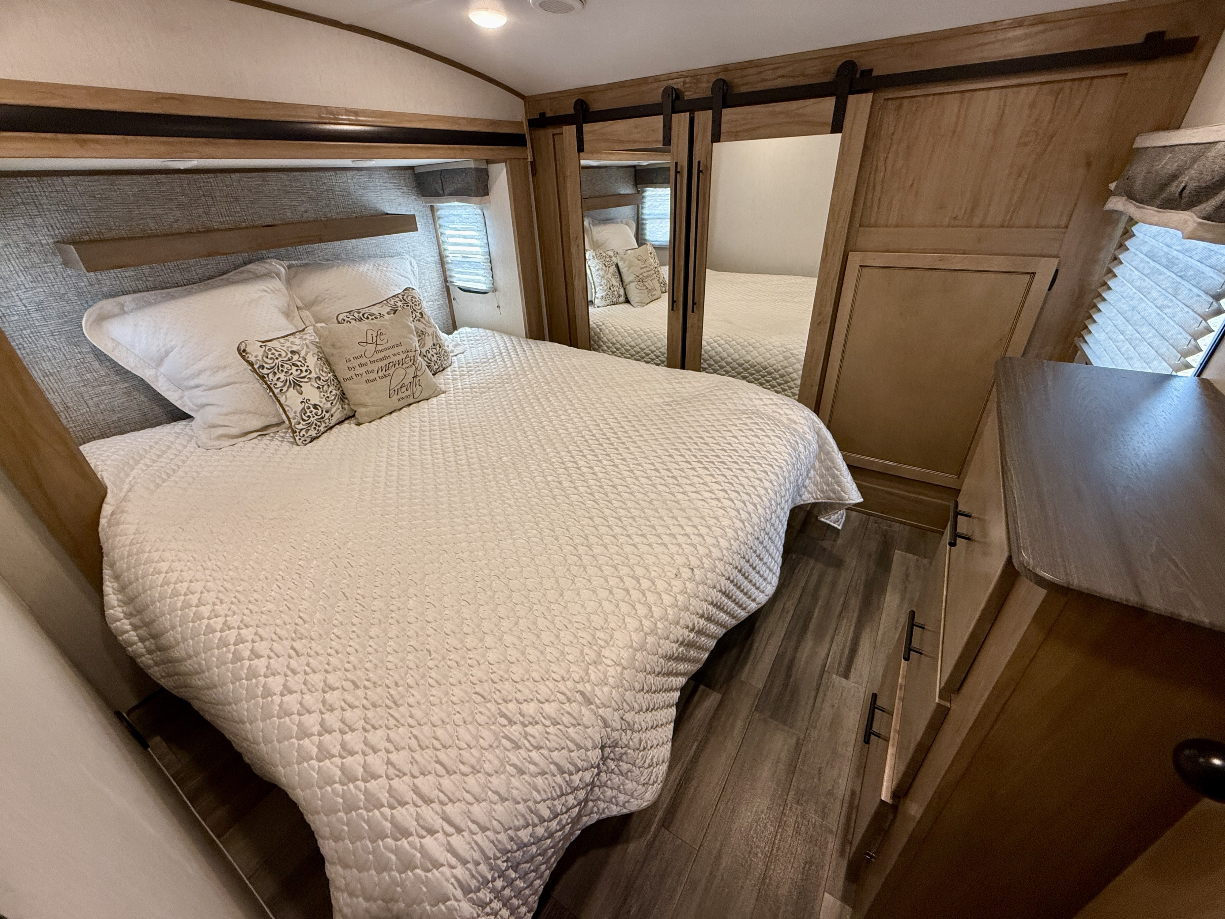 Cozy RV rental bedroom featuring a comfortable bed, mirrored closet, and wood flooring, perfect for your next adventure.. Forest River Sabre 2023