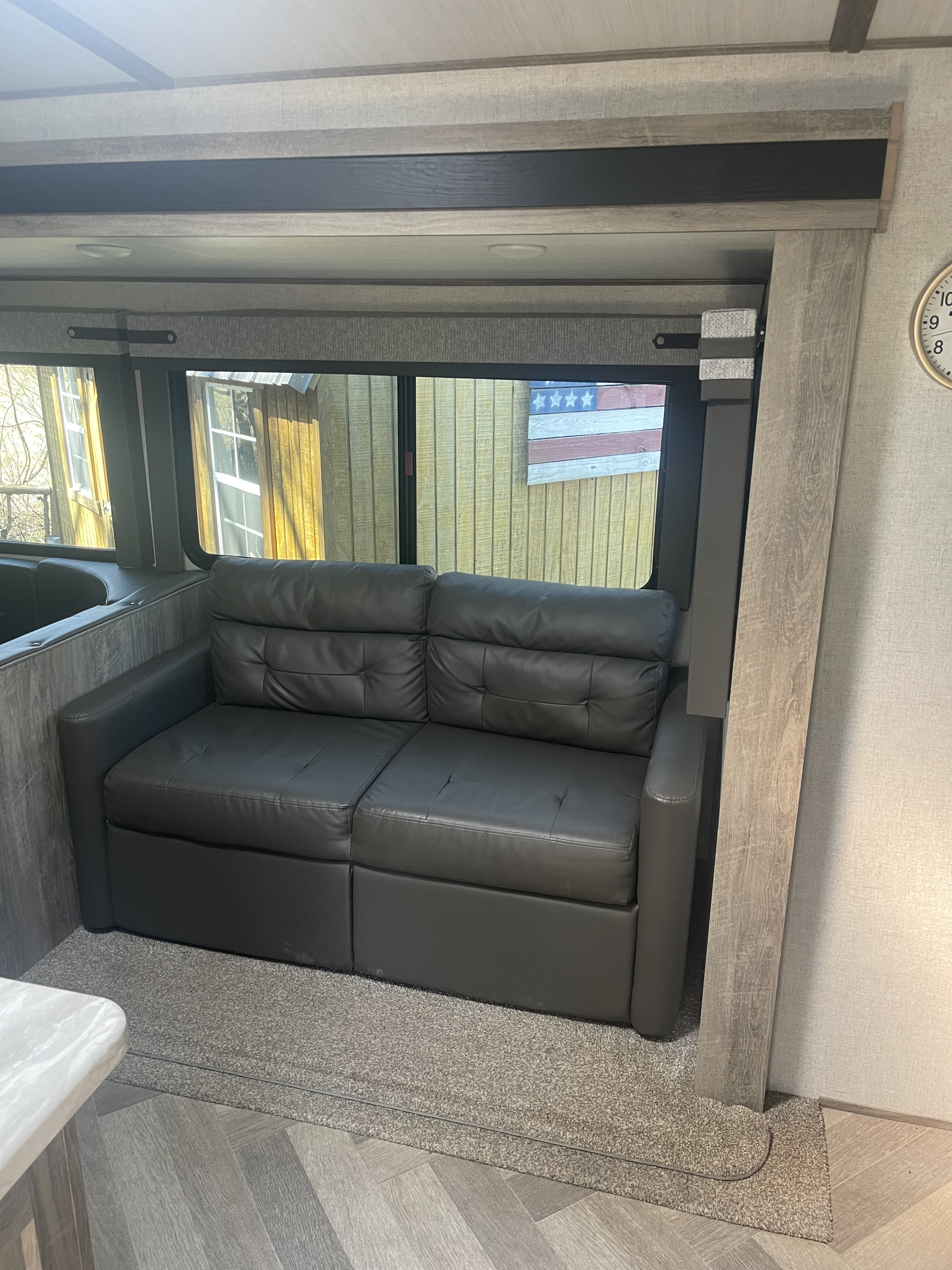 Inside an RV rental: a plush sofa by wide windows showcasing a wooden American flag outside.. Forest River Wildwood Heritage Glen 2021