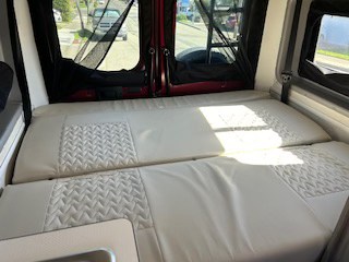 Interior of an RV rental showing a comfortable bed. Sunlight illuminates the quilted cushions, perfect for travel & adventure.. Winnebago Solis 2021